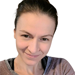 Close-up portrait of a woman smiling with dark hair pulled back, wearing a gray and black top.