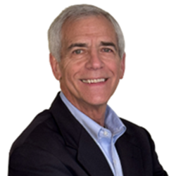An older man with gray hair wearing a dark blazer and light blue shirt, smiling against a white background.