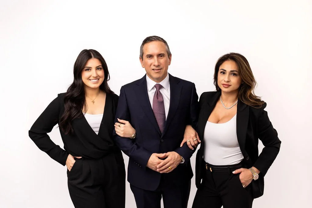 Three professionally dressed individuals, two women and one man, standing against a plain white background, smiling at the camera.