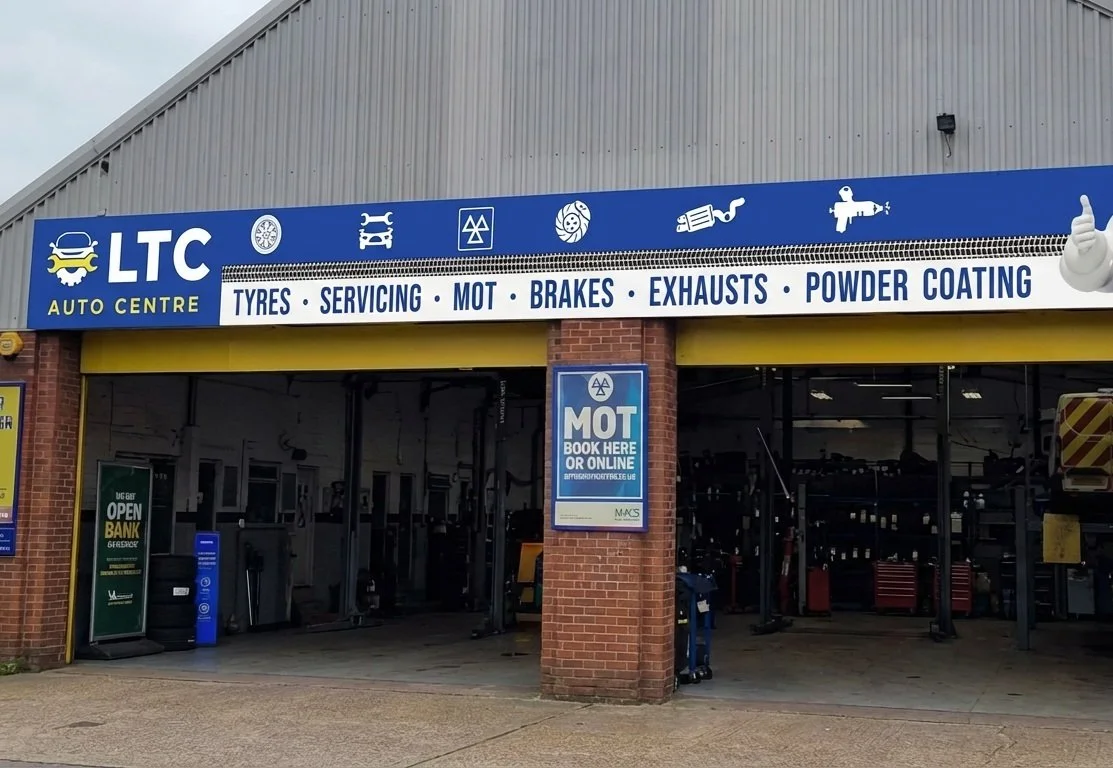 Exterior of LTC Auto Centre with signage indicating services such as tires, servicing, MOT, brakes, exhausts, and powder coating. The building has a brick pillar and a large open garage area.