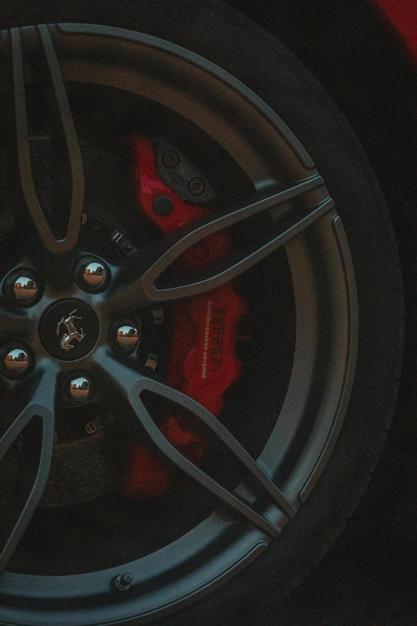 Close-up image of a Ferrari car wheel with a black tire, silver rim, and red brake caliper visible on the inside.