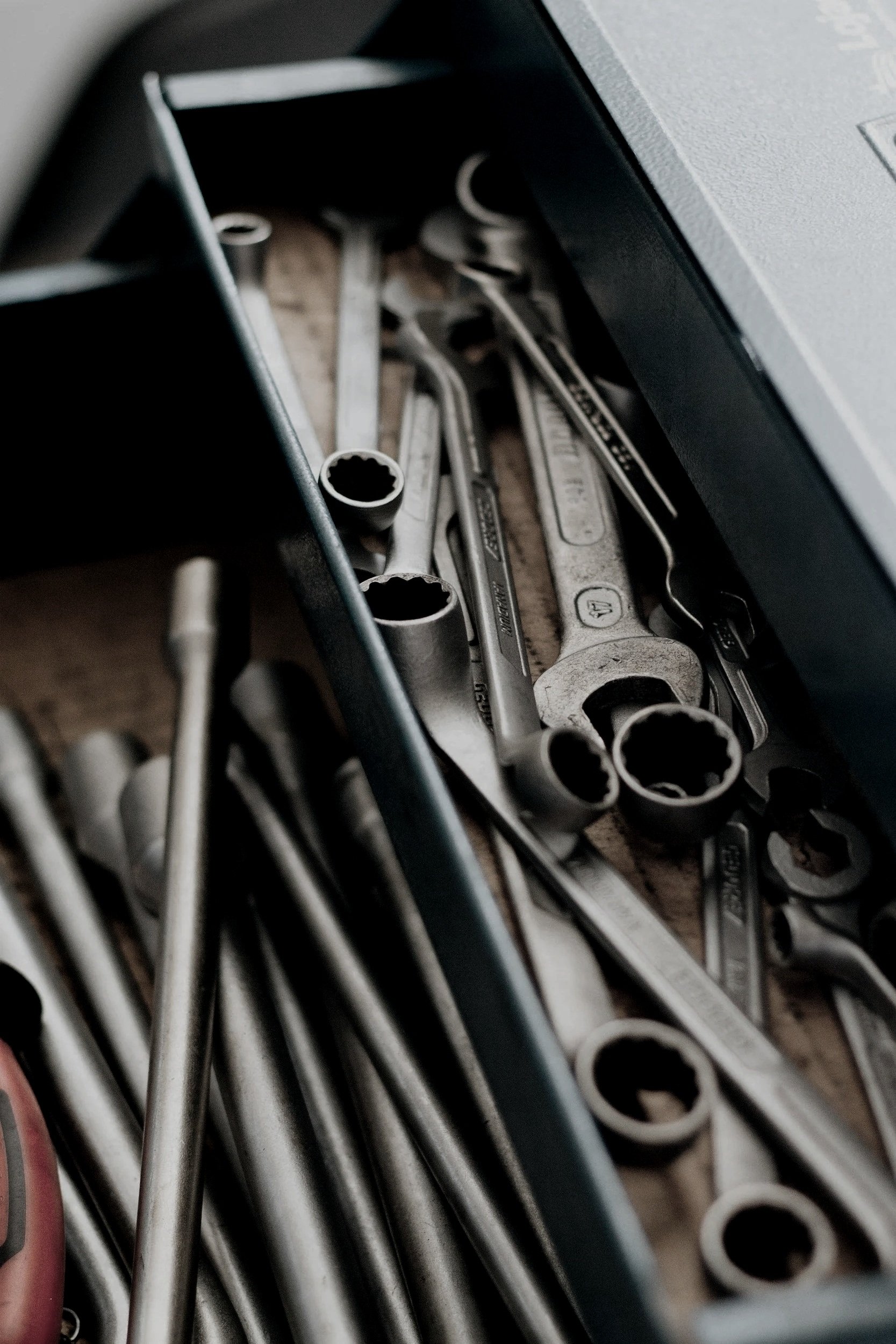 Close-up of a toolbox filled with various metal tools, including ratchet wrenches and Allen wrenches, on a work surface.