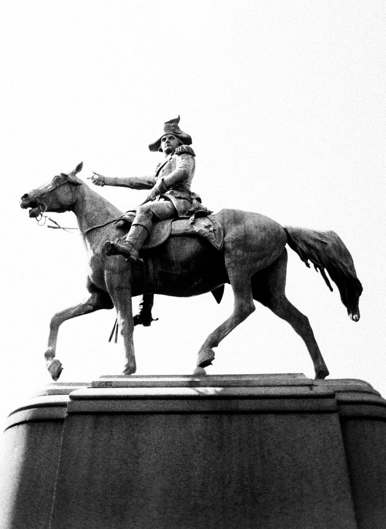 Black and white photo of a statue of a man in military uniform riding a horse, located on a pedestal.