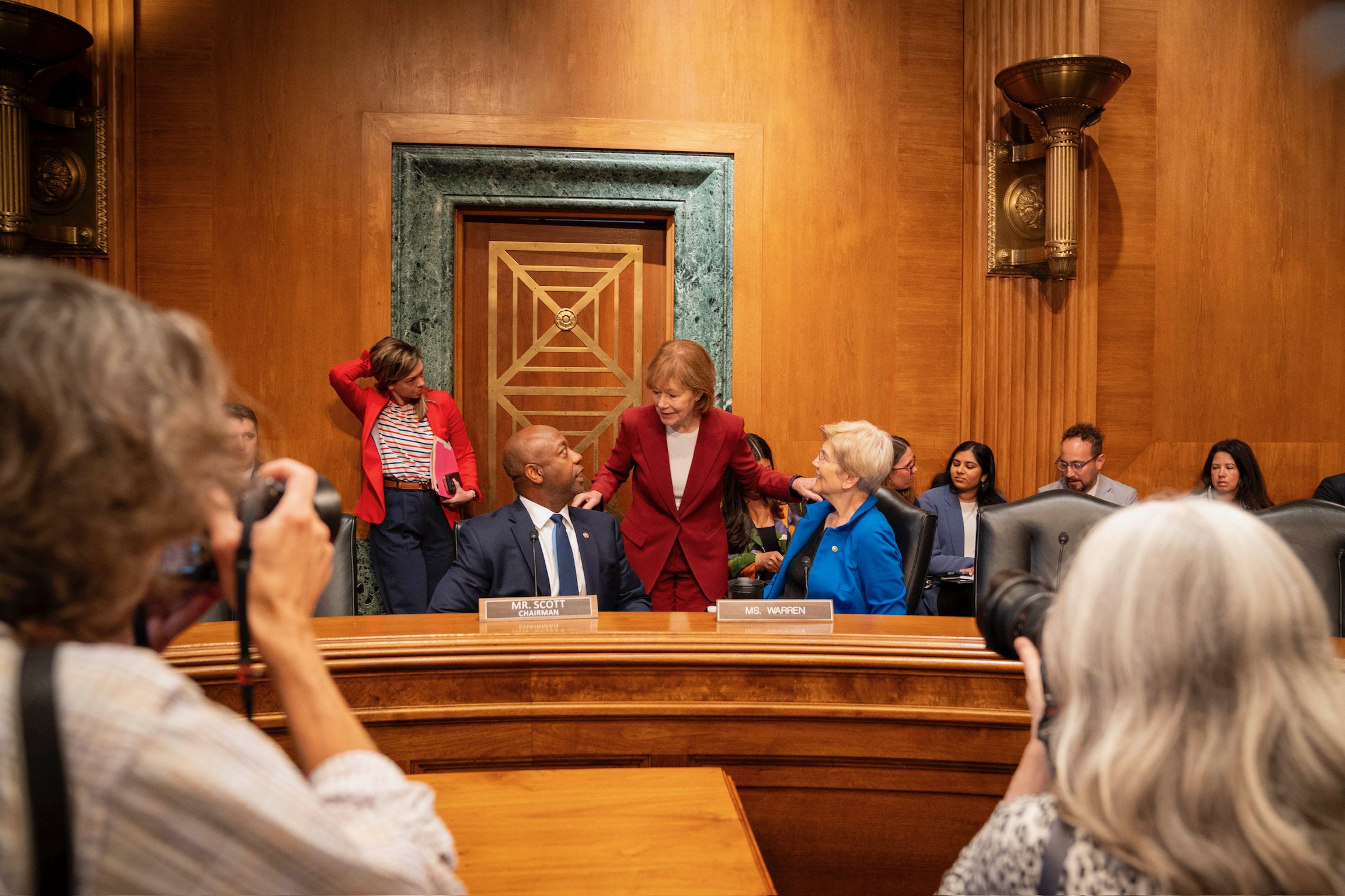 Senators talk together behind the dais in a committee room.