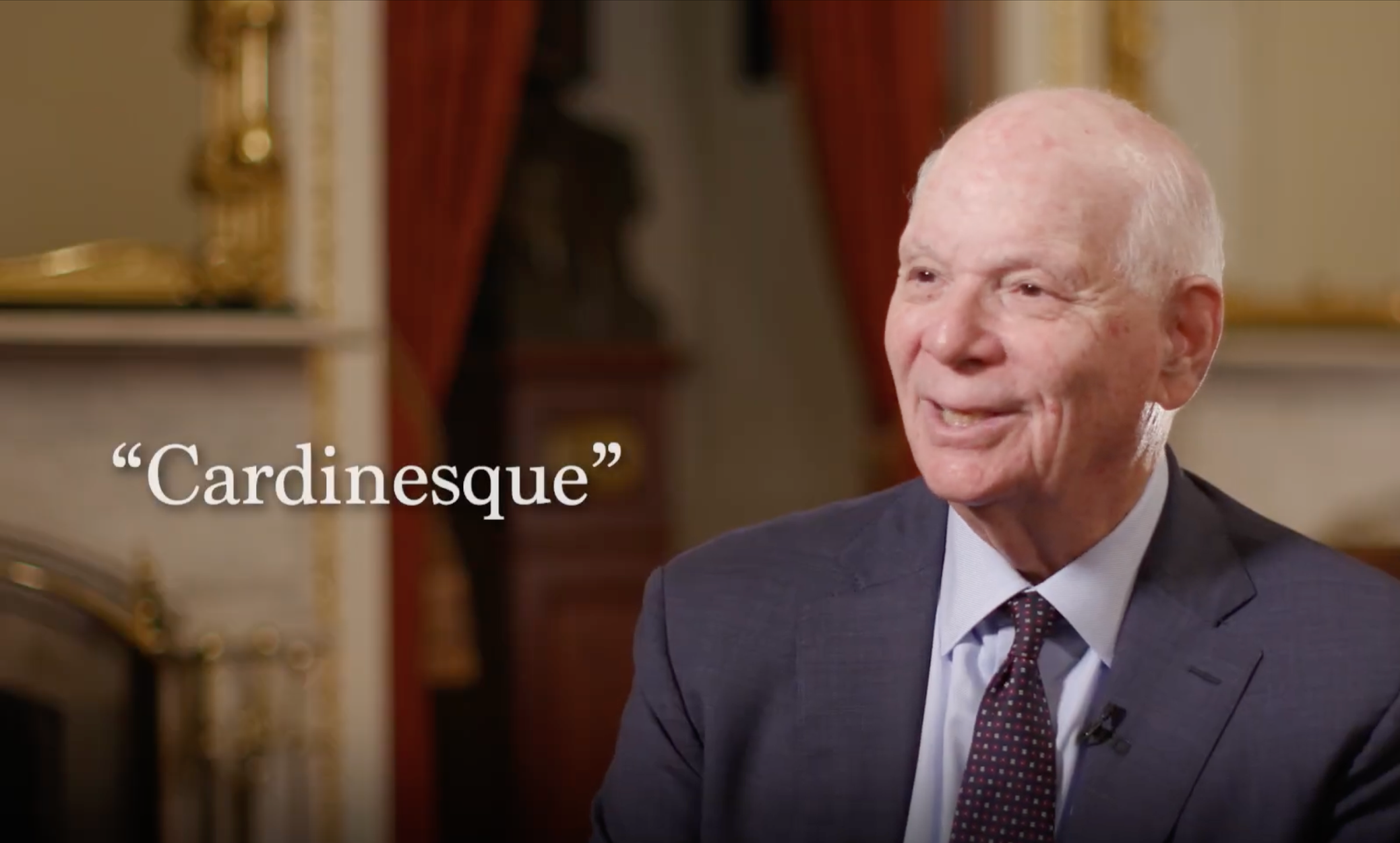 A man with a bald head and light skin in a suit and tie smiling during an interview, with the word "Cardinesque" in white text at the bottom left.