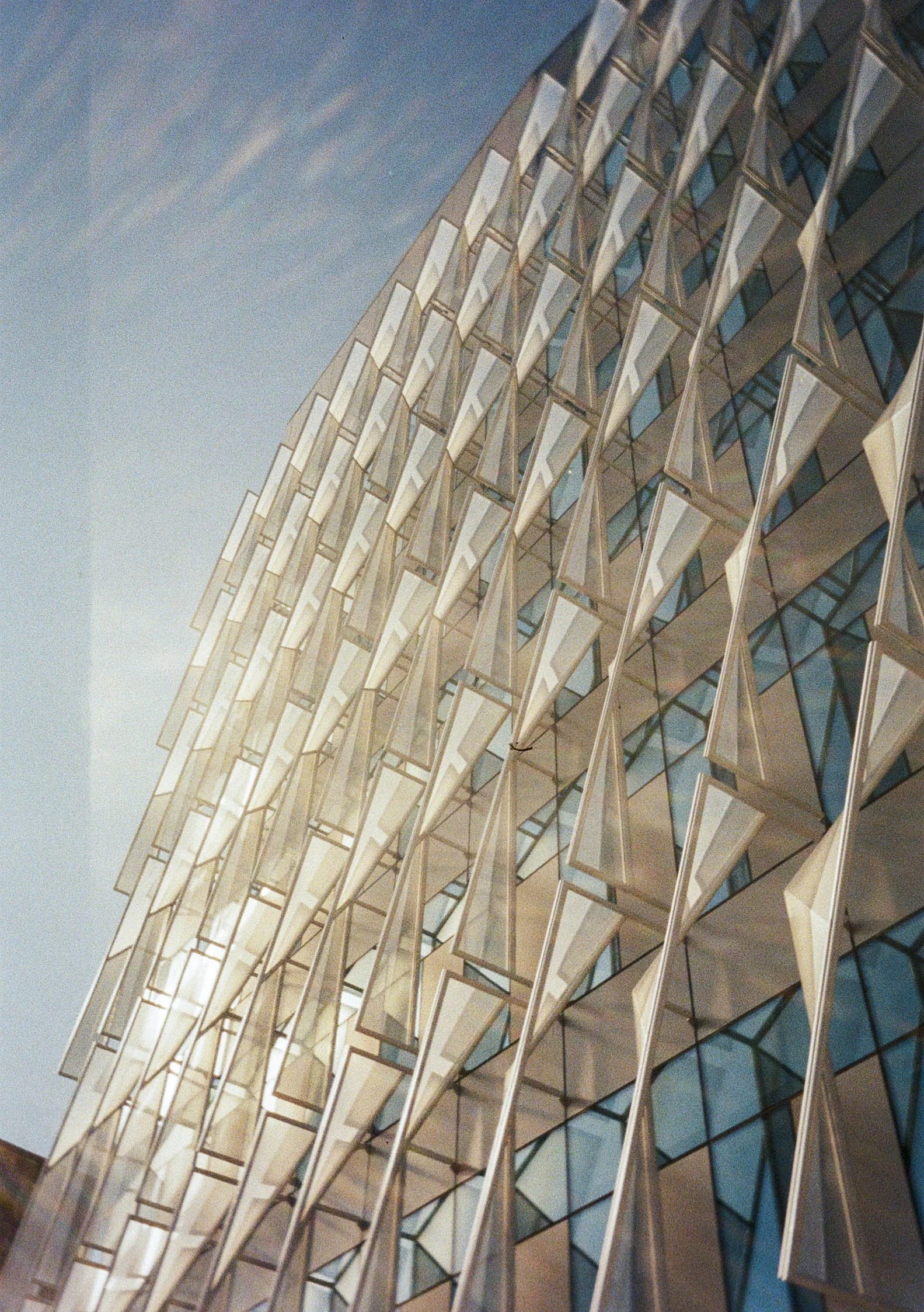 A modern glass and metal building with a distinctive zigzag architectural design, taken from a low angle during dusk.