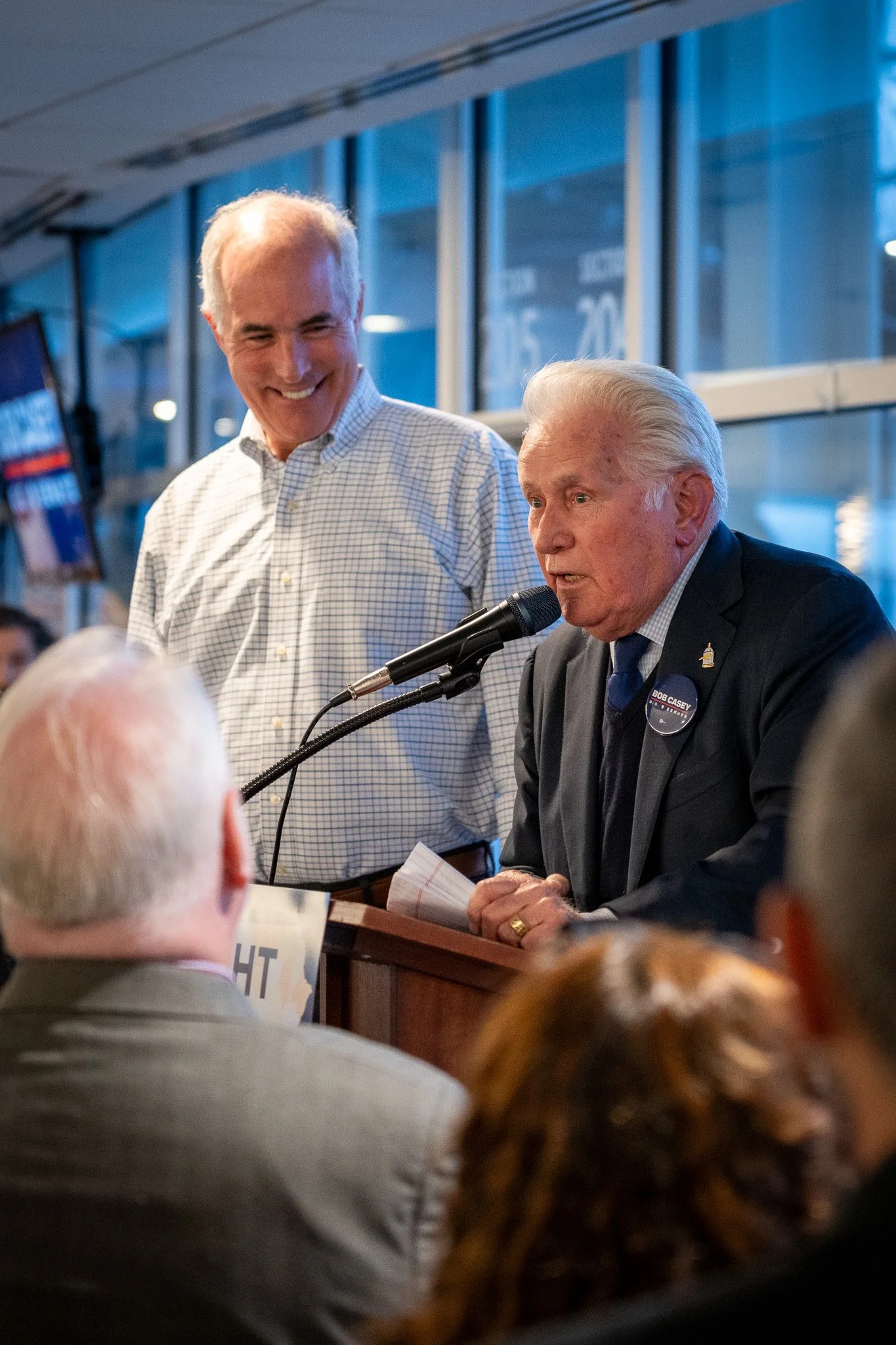 Senator Bob Casey standing behind Martin Sheen, speaking at a campaign event.