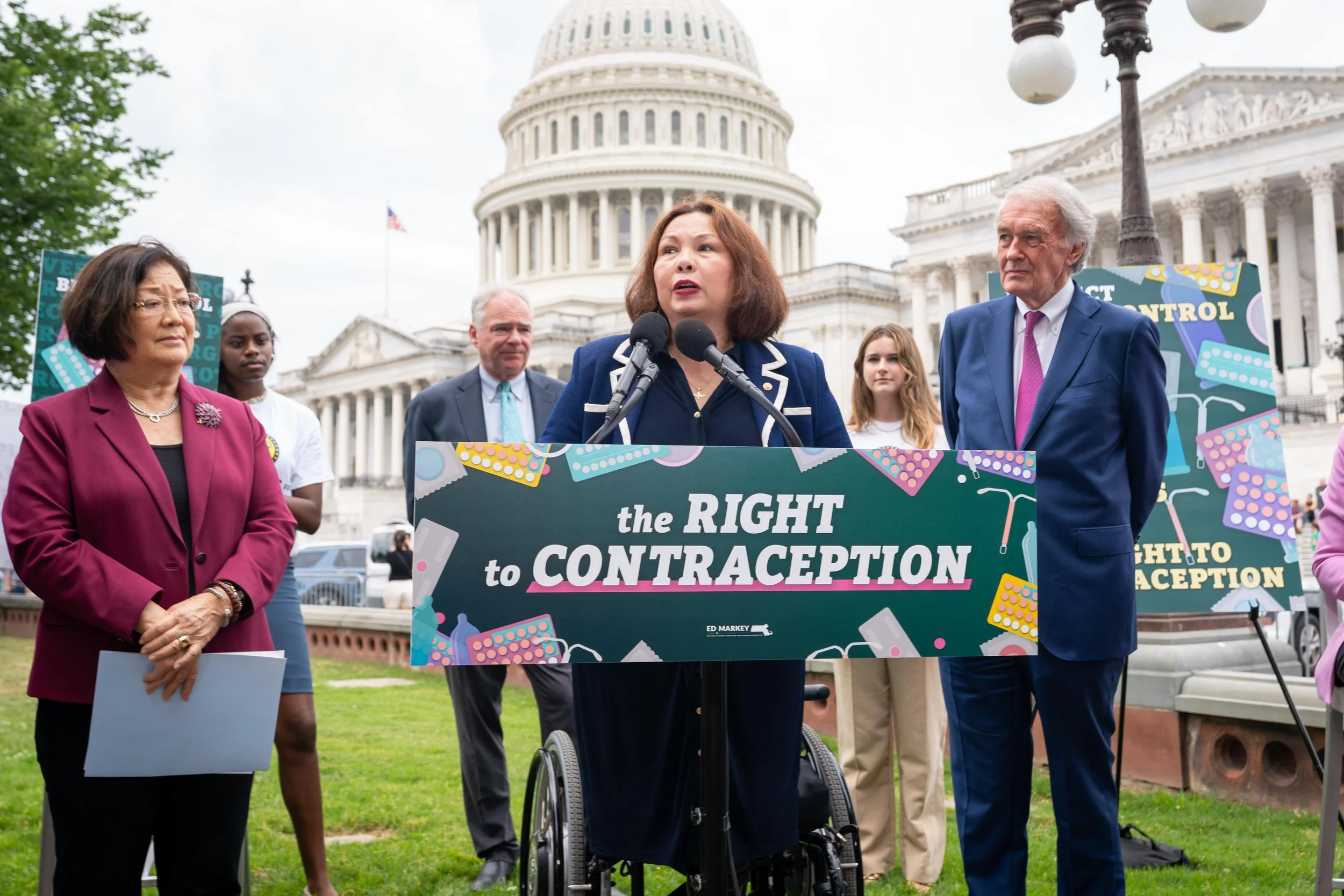 Senators speaking at a rally outside the U.S. Capitol building with a sign advocating for contraception rights.