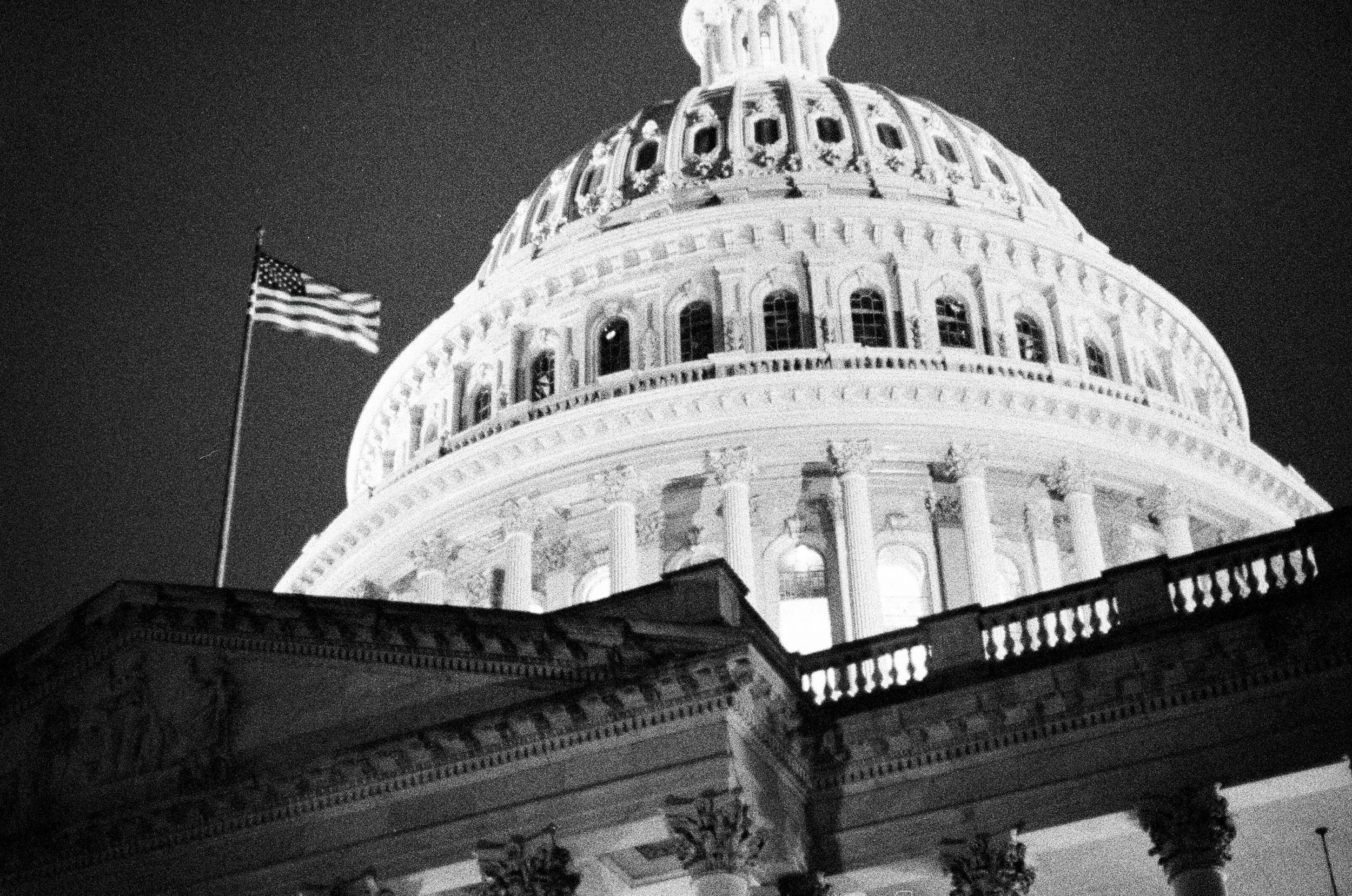 Nighttime view of the United States Capitol building with an American flag flying nearby.
