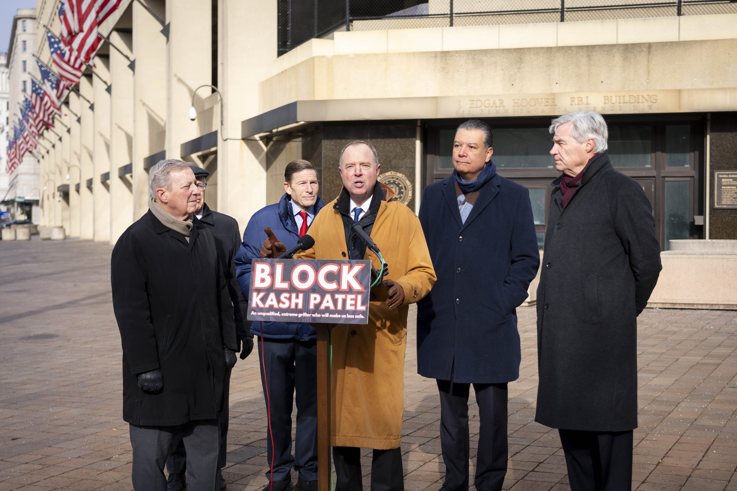 Senators speaking at a press conference in front of the FBI building, with a sign that says "Block Kash Patel."