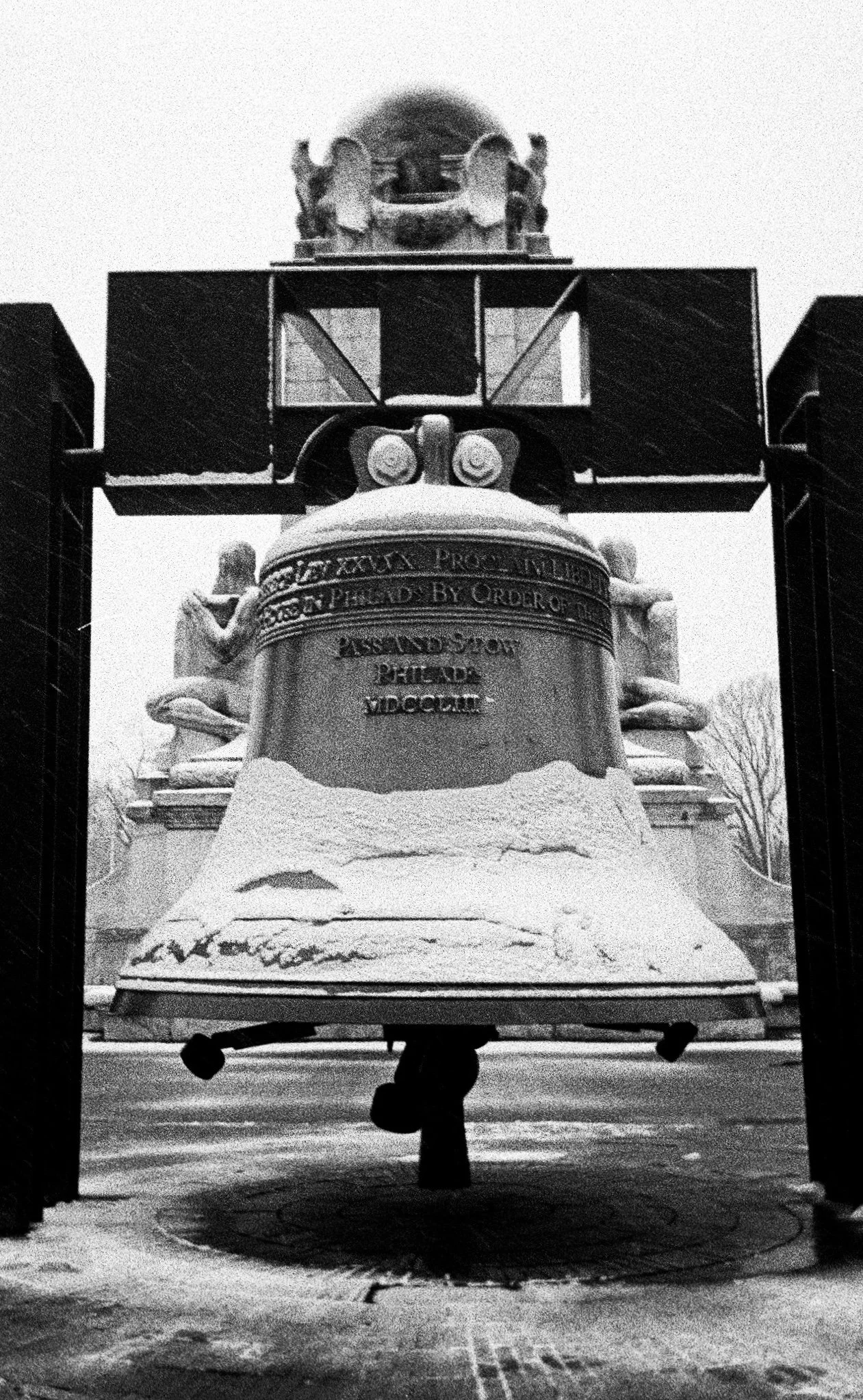 A black and white photograph of a large statue of a lion holding a circular plaque with inscriptions, topped with a structure that resembles an aircraft. The scene is icy with snow on the ground.