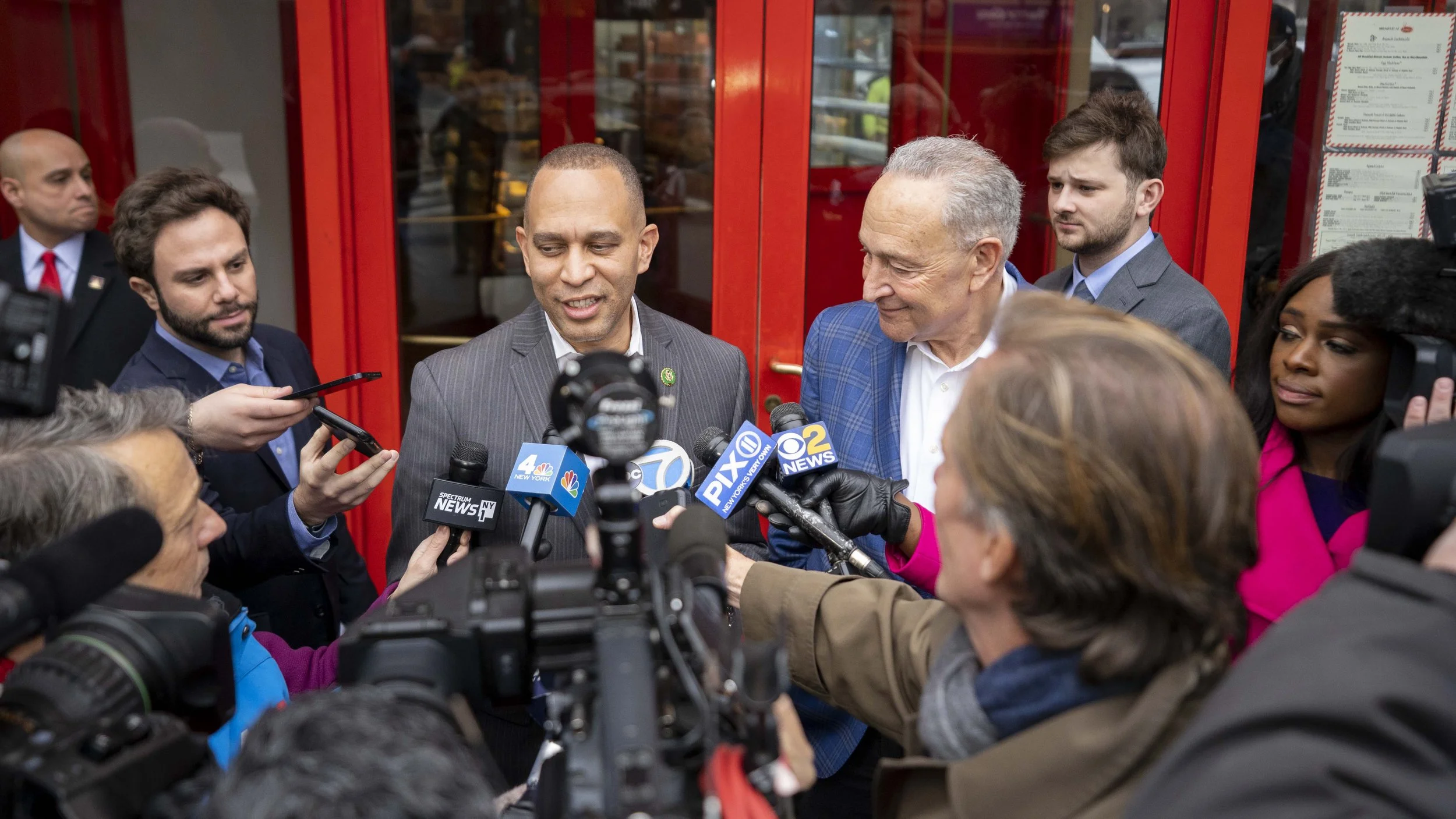 Hakeem Jeffries and Chuck Schumer, speaking to the media outside Junior's, with microphones from news stations in front of them.