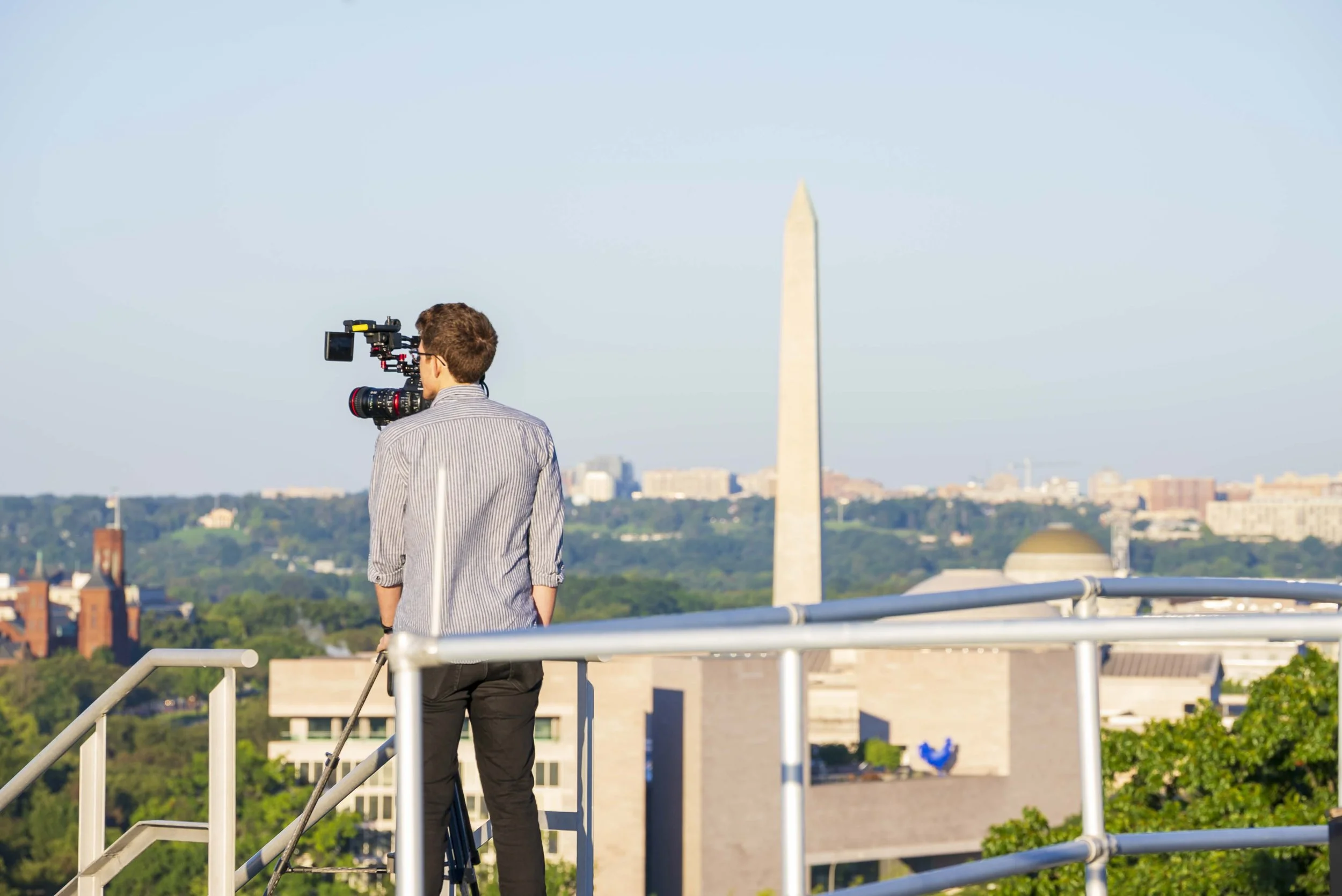 Brooks operates a video camera on the rooftop of the Senate Russell Office Building, with the Washington Monument in the background during daytime.