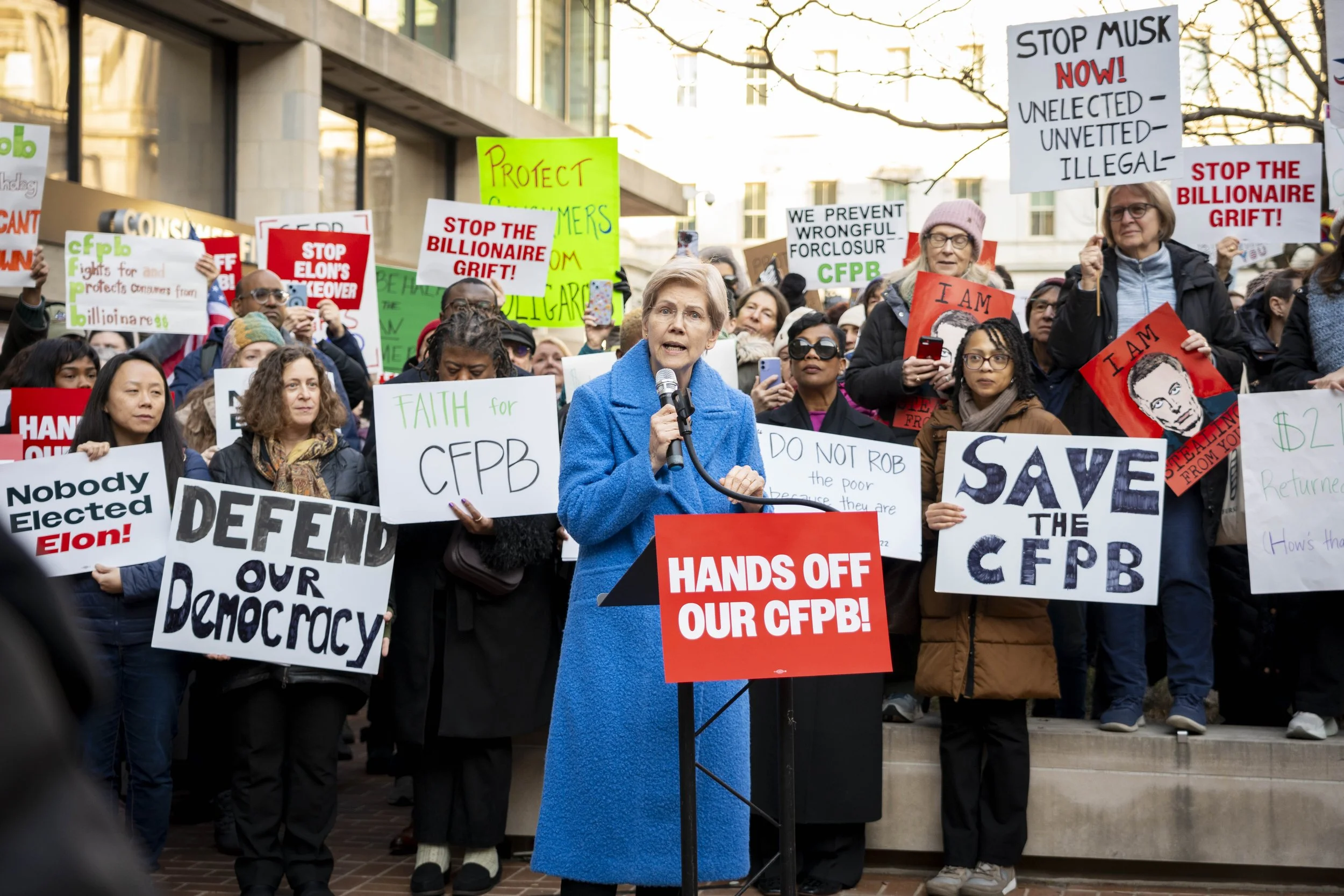 Sen. Elizabeth Warren speaks to a crowd holding signs in front of the CFPB.