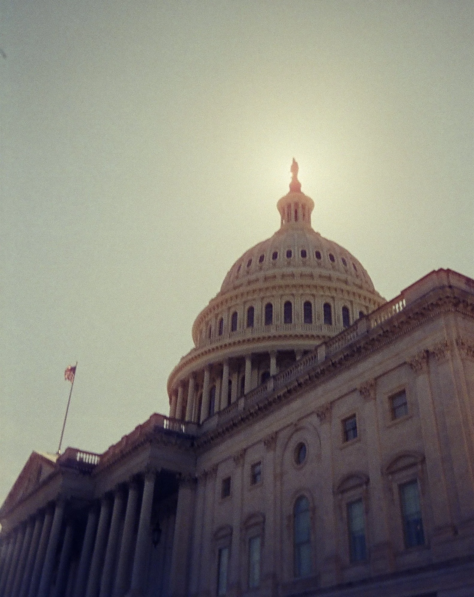 Upside-down view of the United States Capitol building with an American flag flying on a flagpole, against a dimly lit sky during sunset or sunrise.