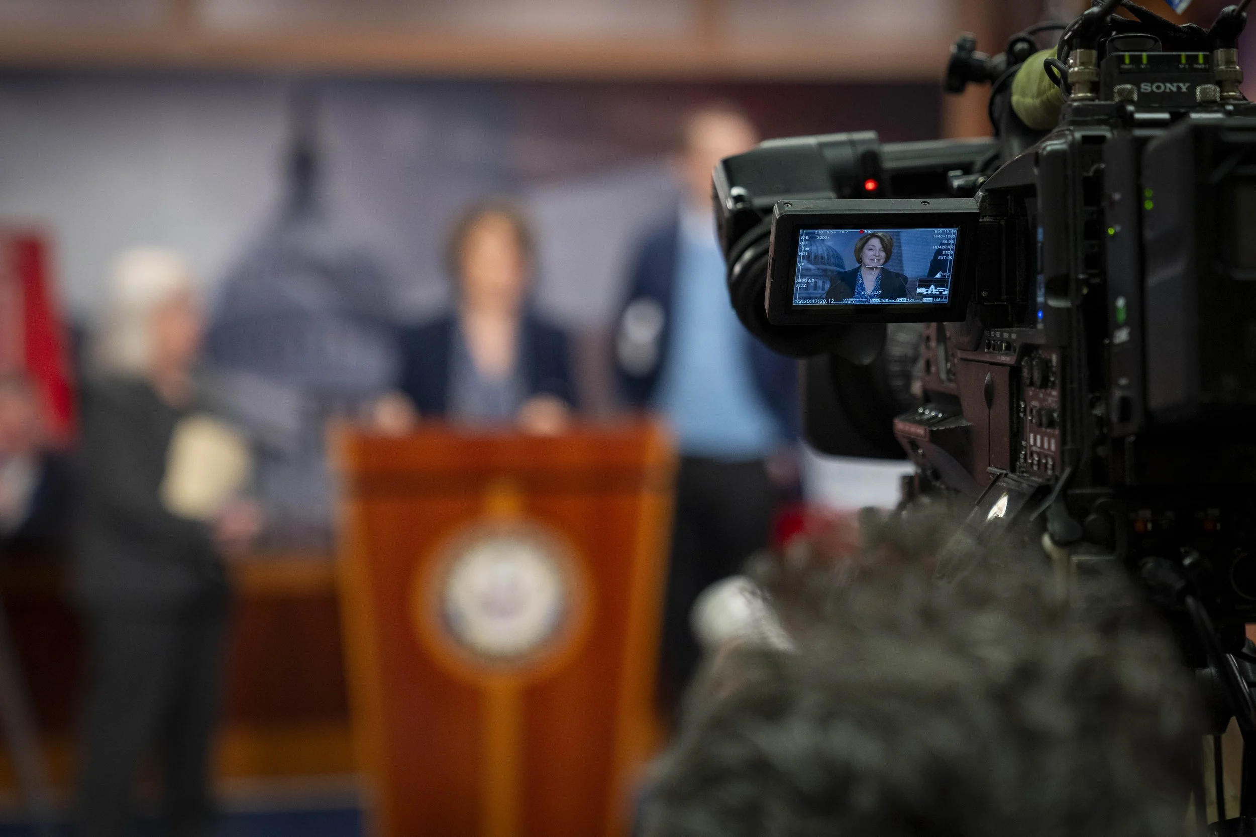 Sen. Amy Klobuchar on a TV screen being recorded by a professional camera in a press conference.
