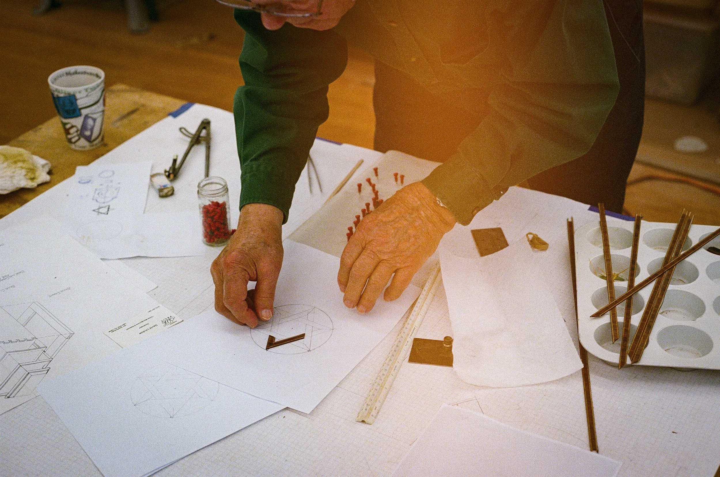 Person working on architectural or engineering drawings at a desk with various tools and materials.