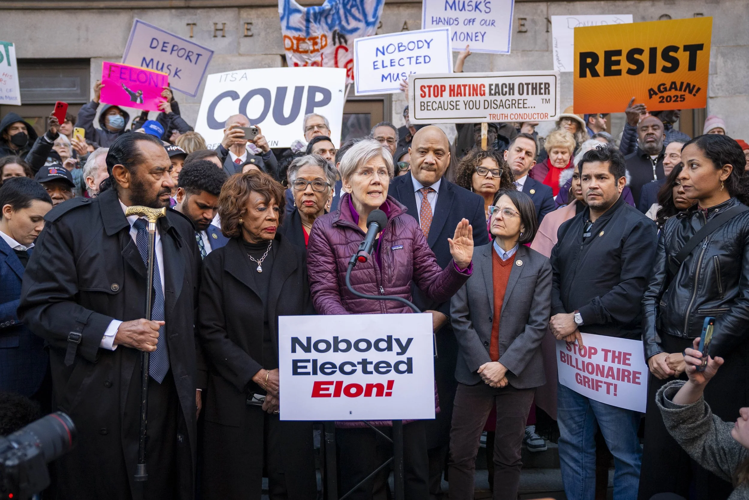 Sen. Elizabeth Warren speaks to a crowd in front of the Treasury Department with a sign that says "Nobody Elected Elon!"