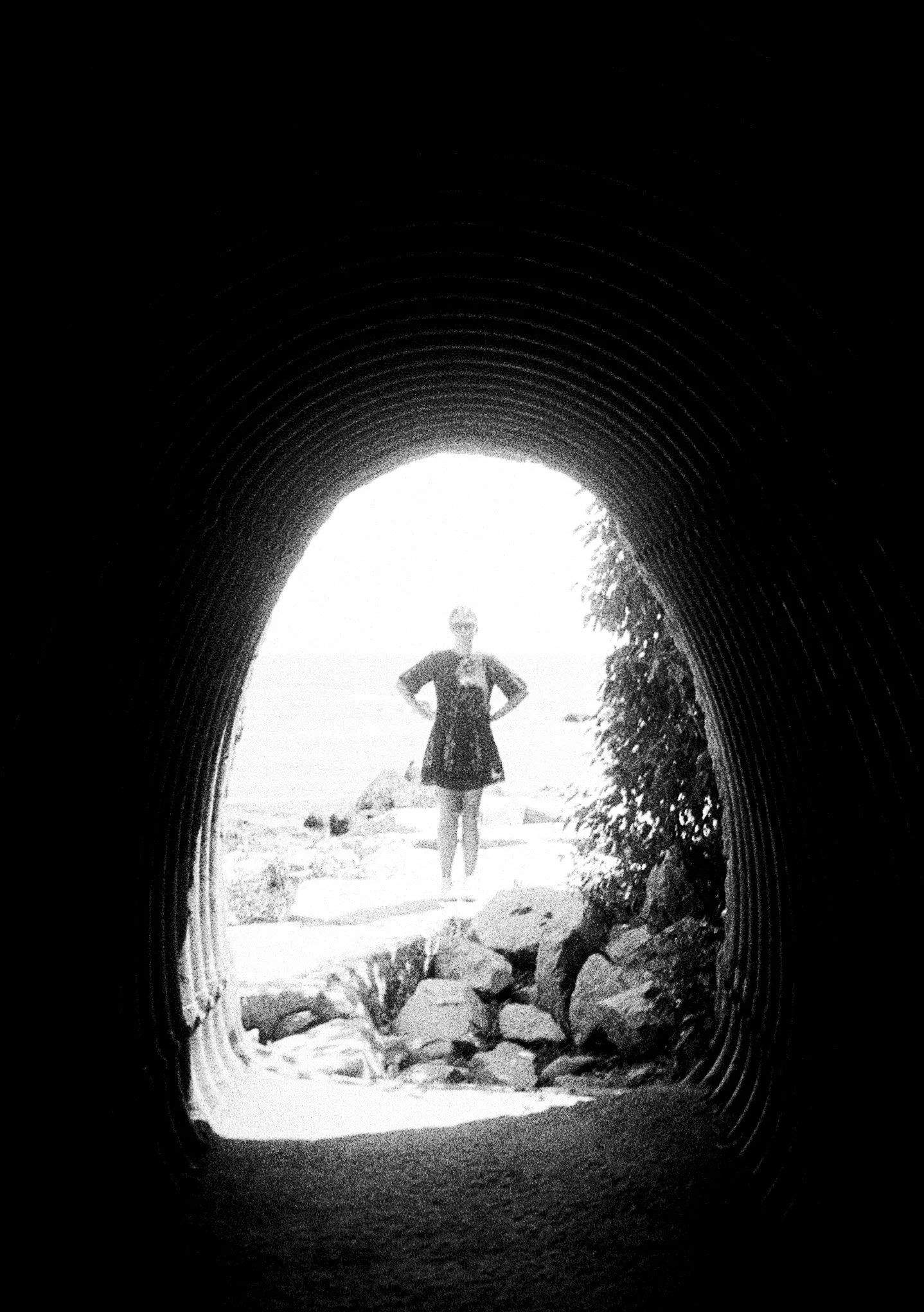 Person standing in front of a river in a cave or tunnel with rocks and trees visible outside.