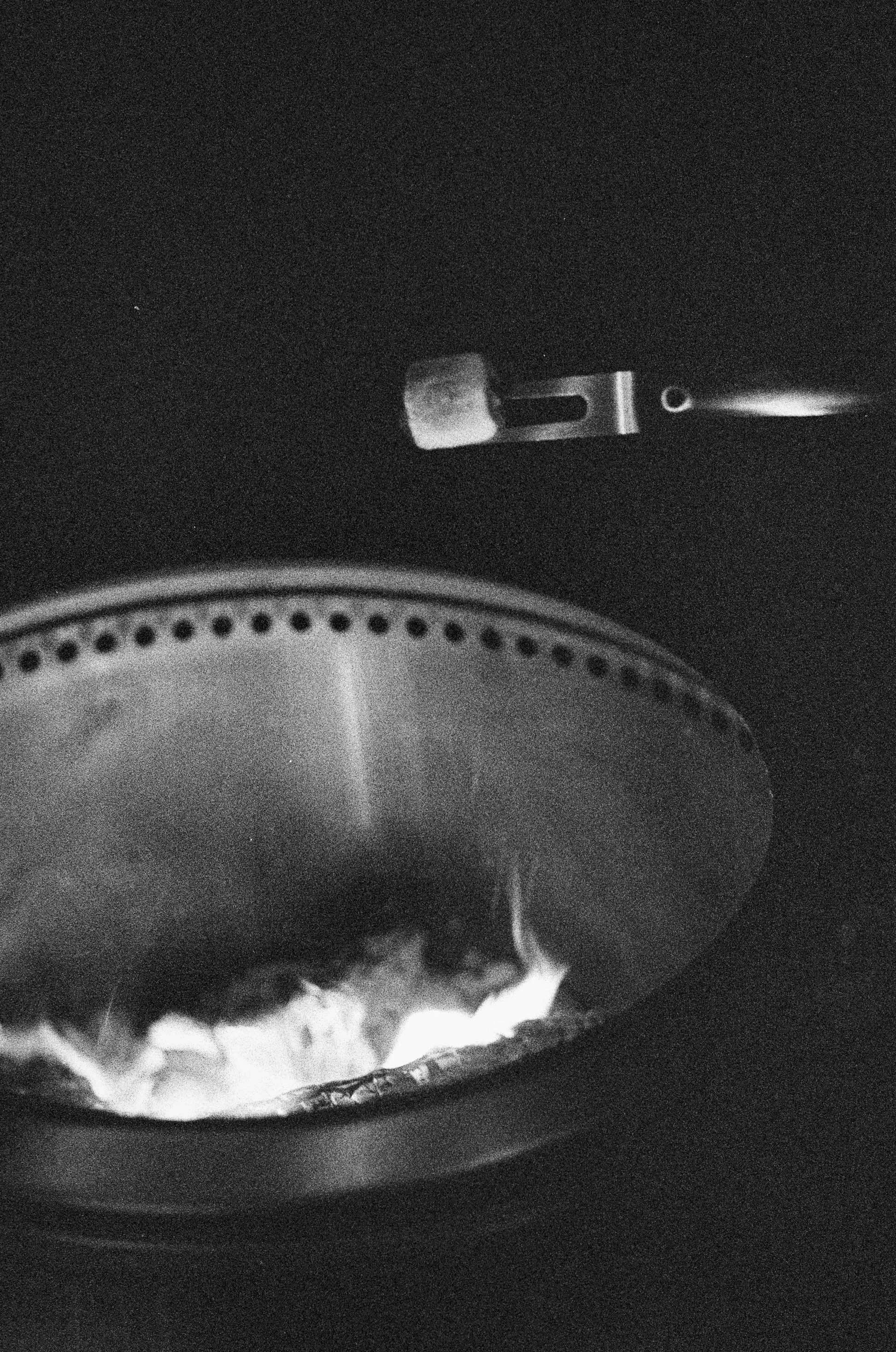 A close-up of a metallic razor blade hot in a fire, with part of a metallic object, possibly a jar or can, heated and glowing with a liquid or substance inside.
