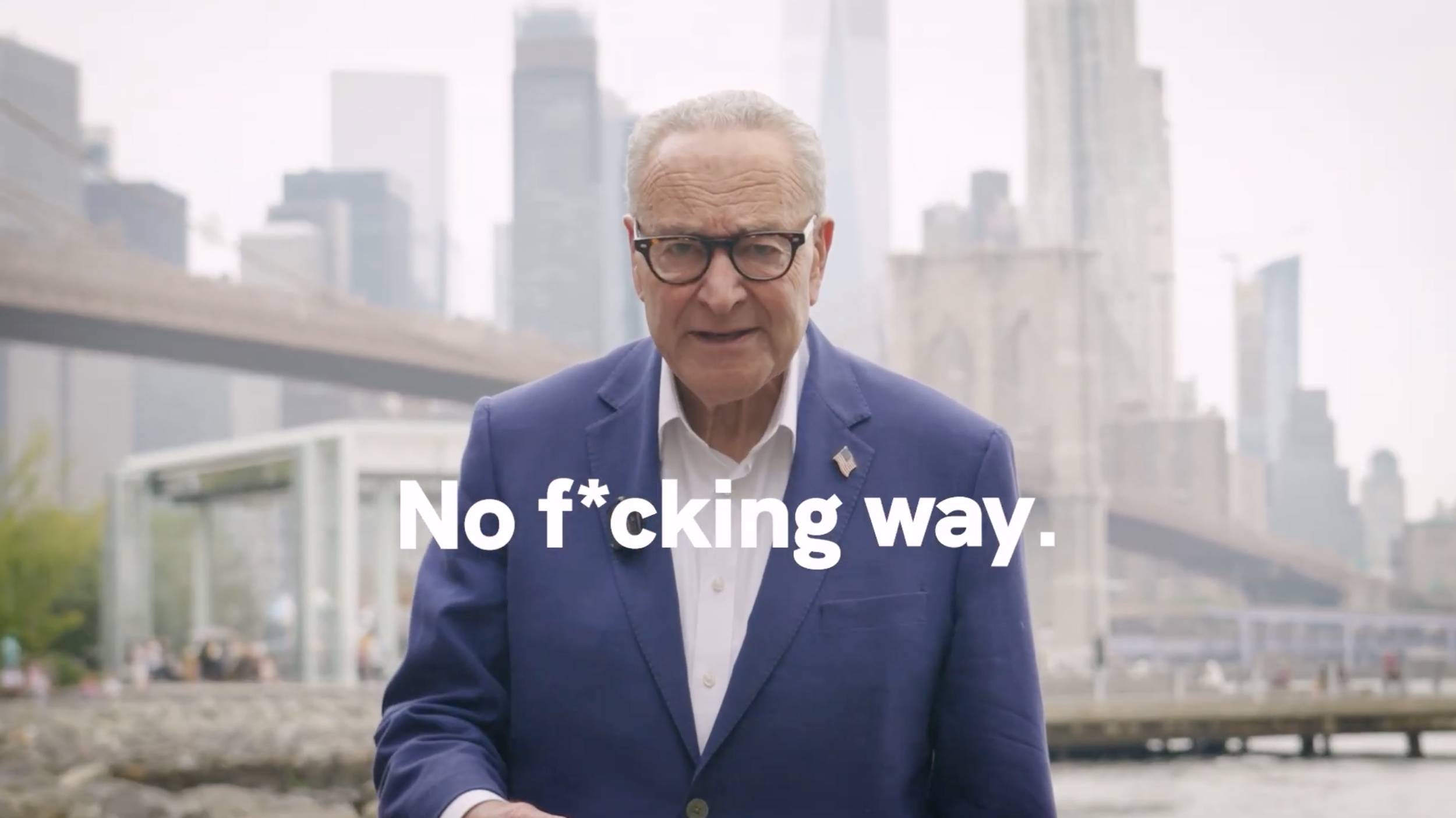 An older man with gray hair and glasses, wearing a blue suit jacket and a white shirt, standing outdoors in front of a cityscape with tall buildings. He has a serious expression and the caption says, "No f*cking way."