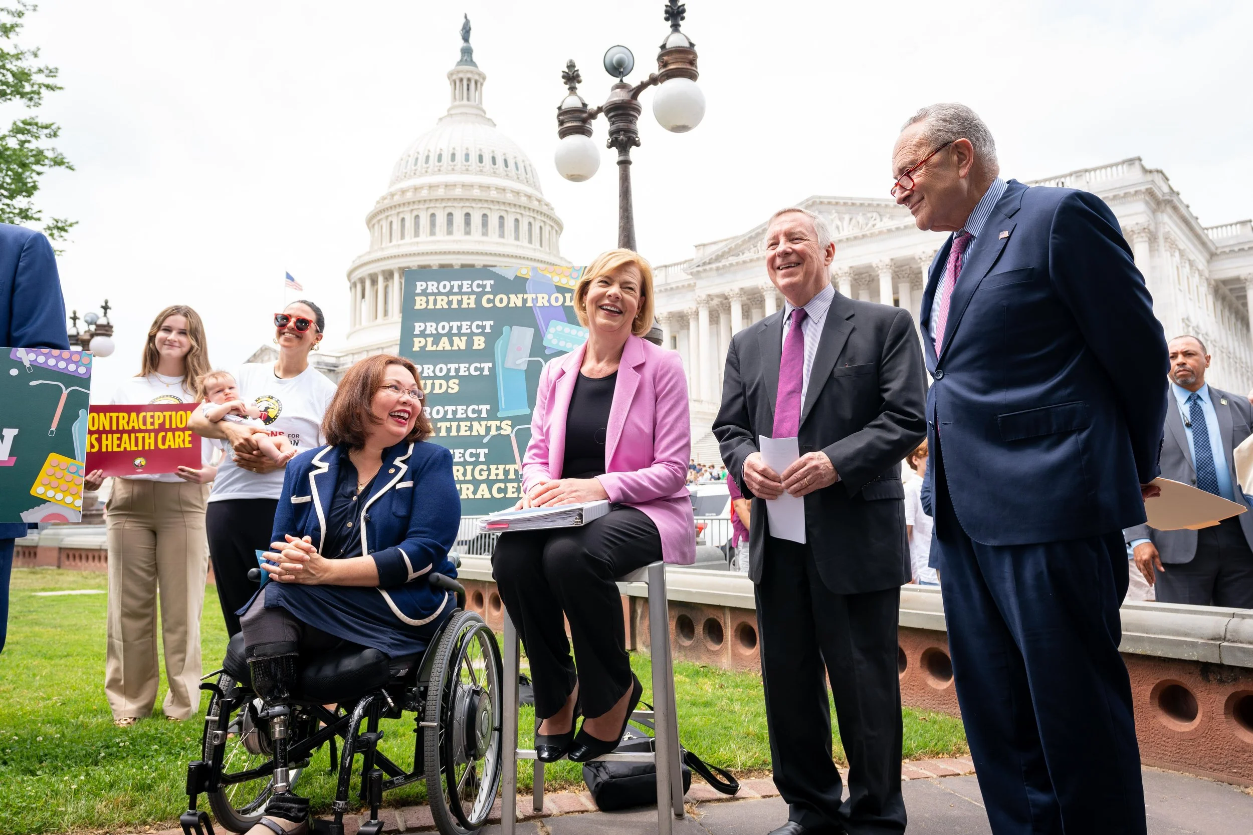 Senators smile at each other at a press conference in front of the US Capitol.