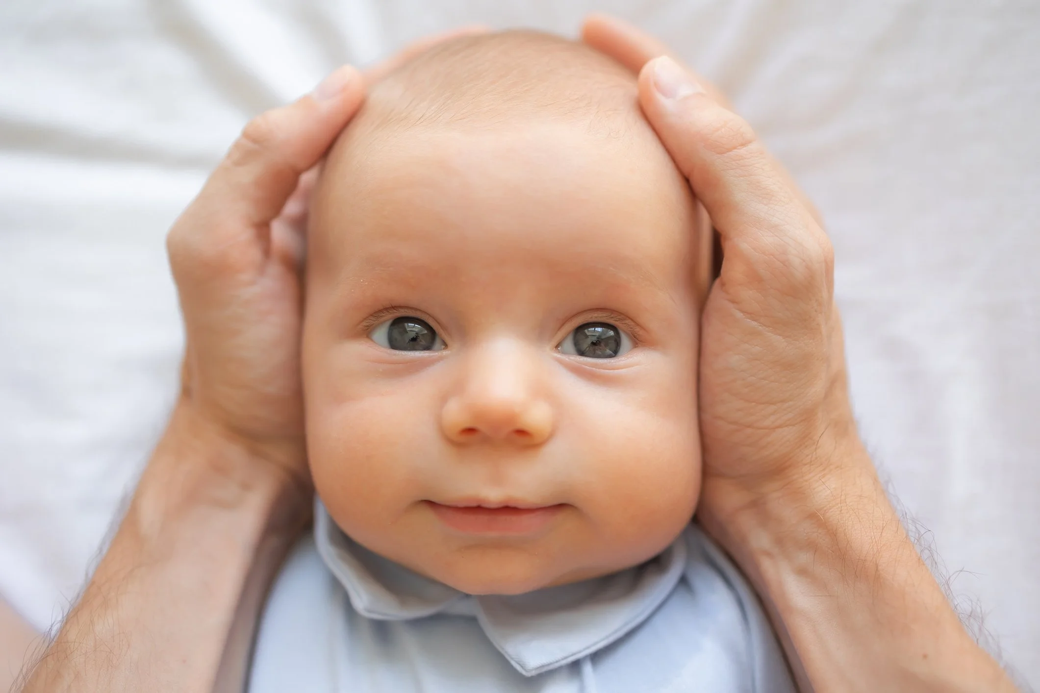 an infant stares straight ahead happily as its head is cradled by two adult hands