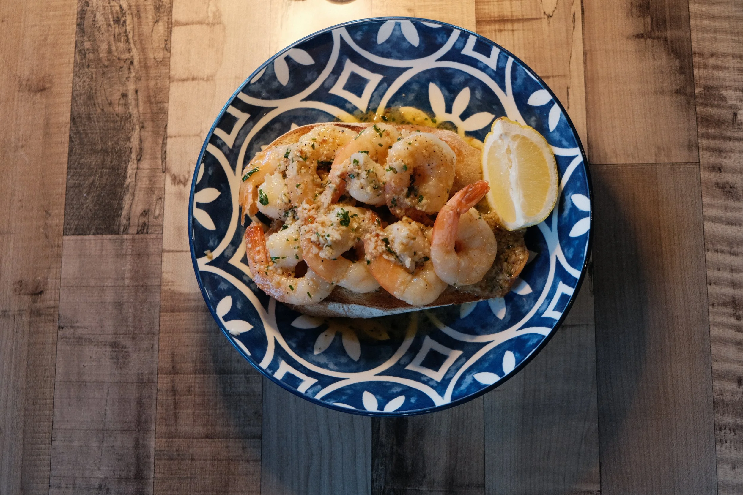 A plate of shrimp and toast with a lemon wedge on a wooden table.