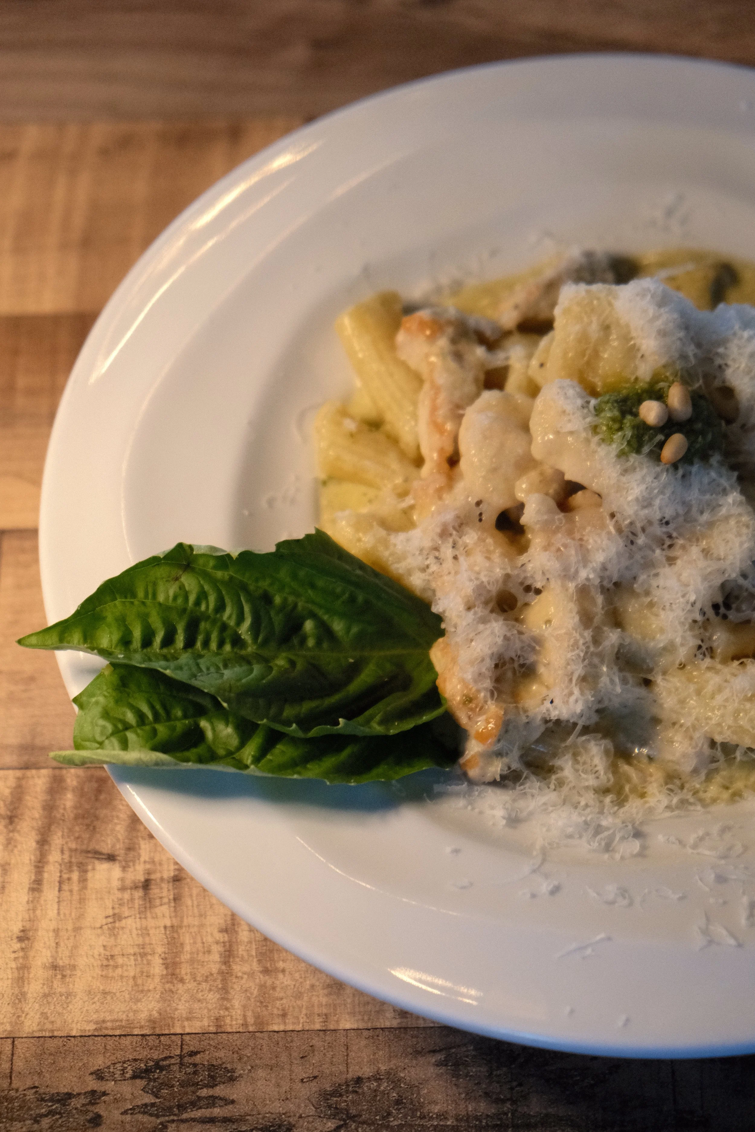 Close-up of a plate of pasta with creamy pesto sauce, cheese, garnished with fresh basil leaves on the side.