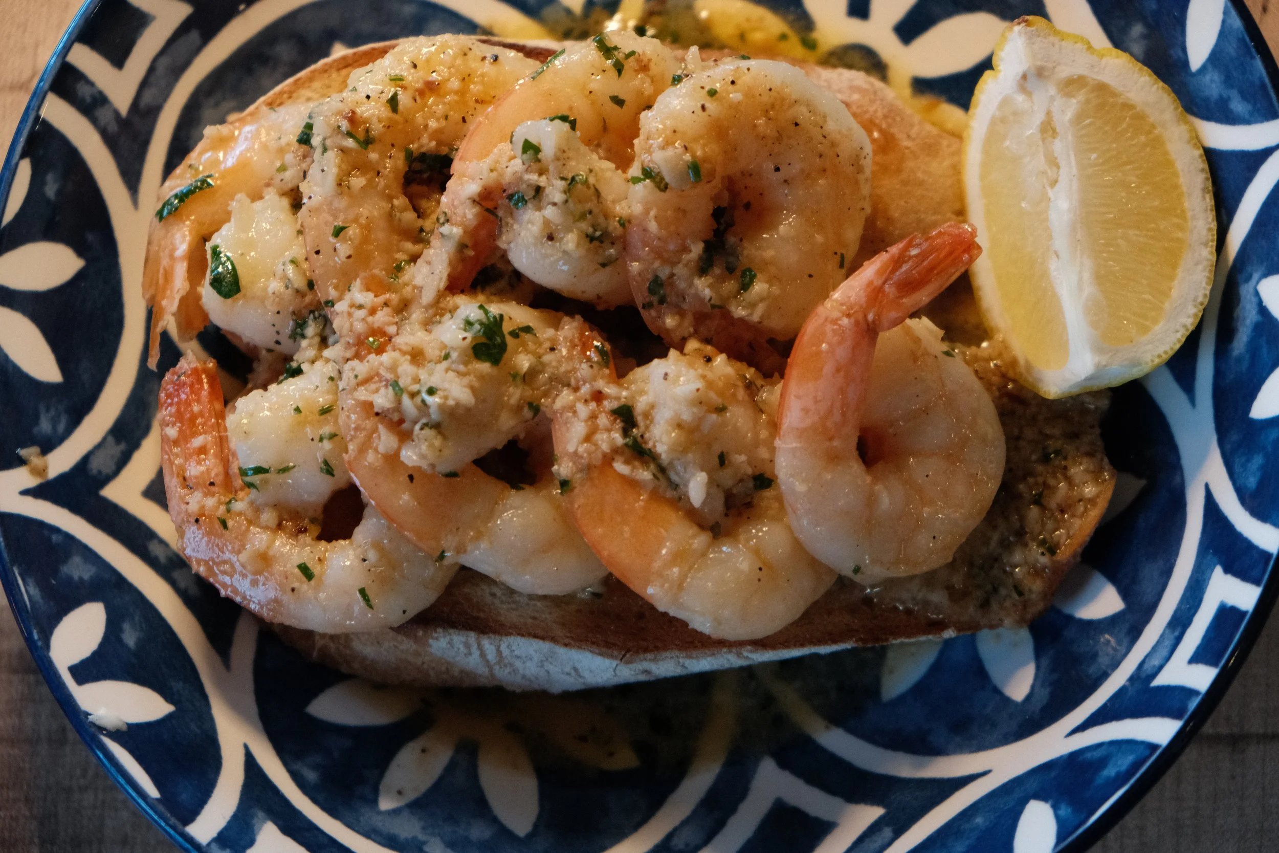 Shrimp appetizer served on toasted bread with lemon wedge on a decorative plate.