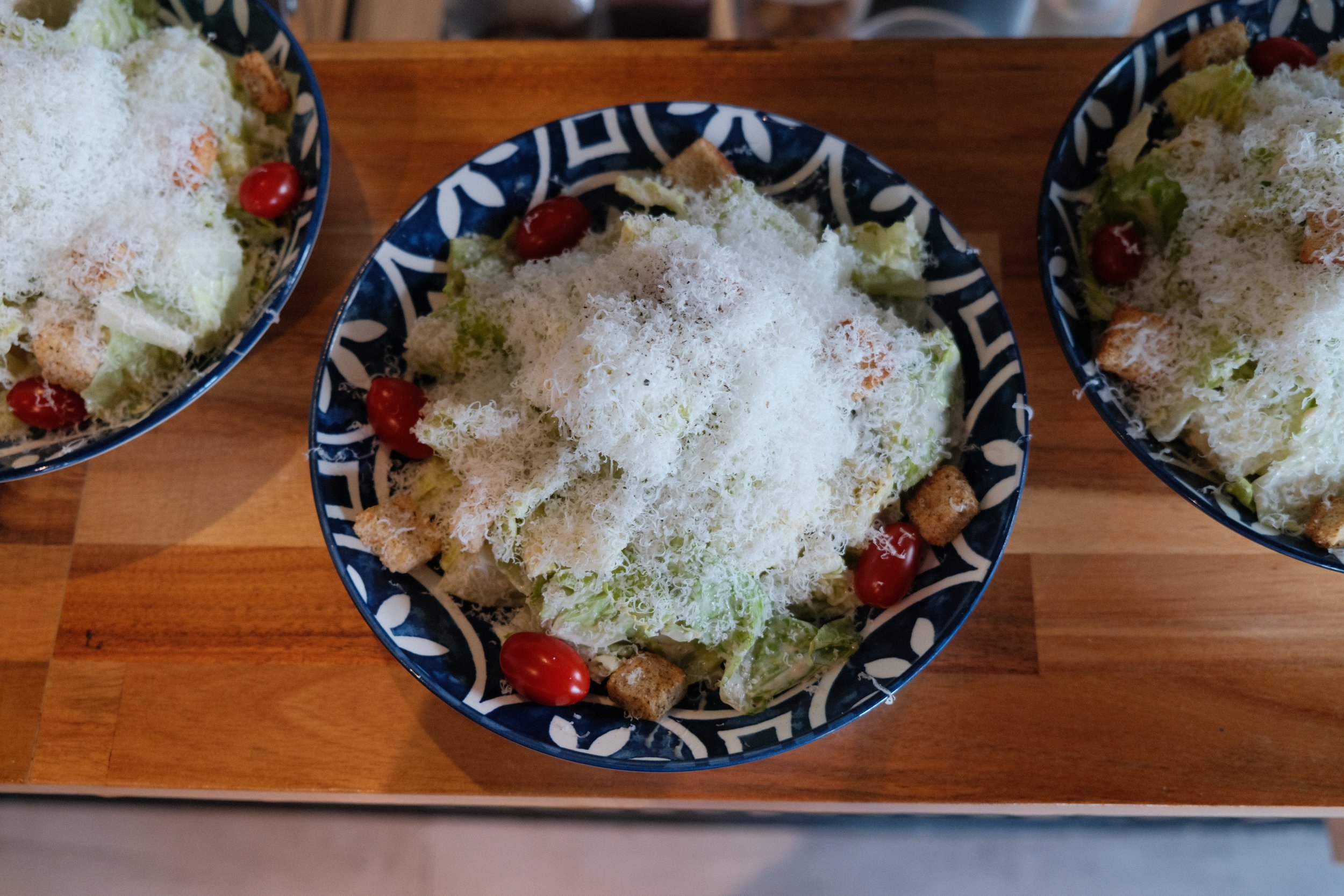 A Caesar salad topped with shredded cheese and cherry tomatoes, placed on a wooden table.