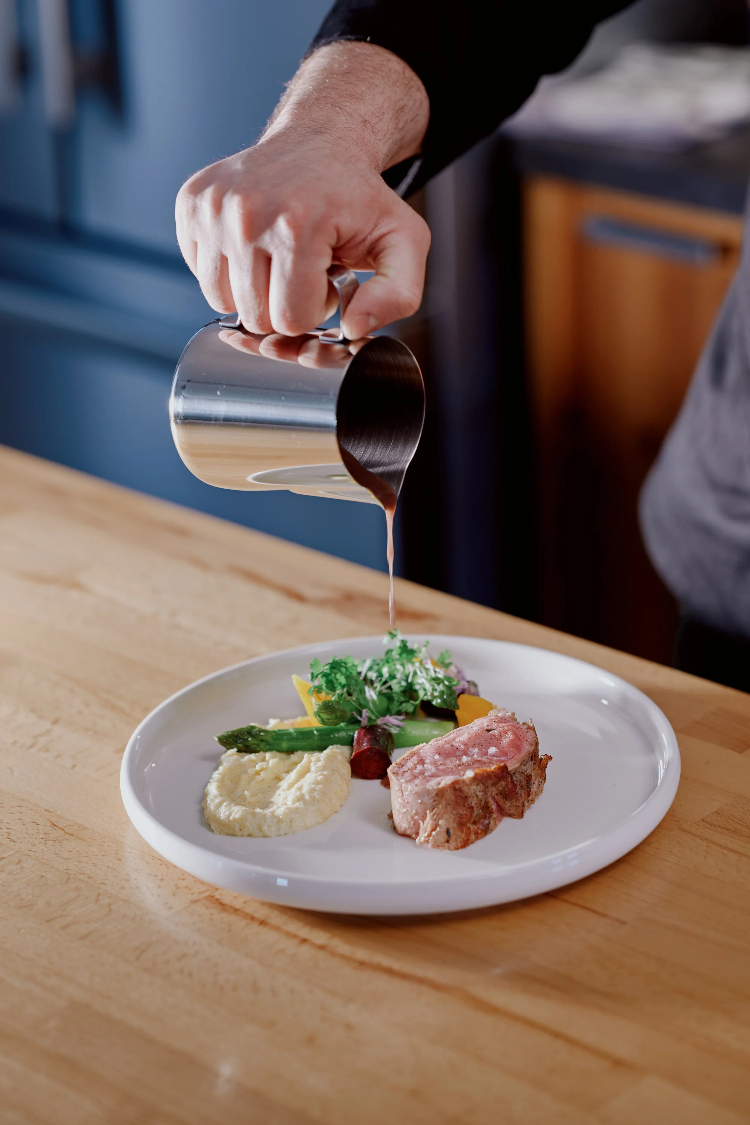 Un plat avec de la viande, de la polenta, des légumes et une sauce, étant servi avec de la sauce sur une table en bois.