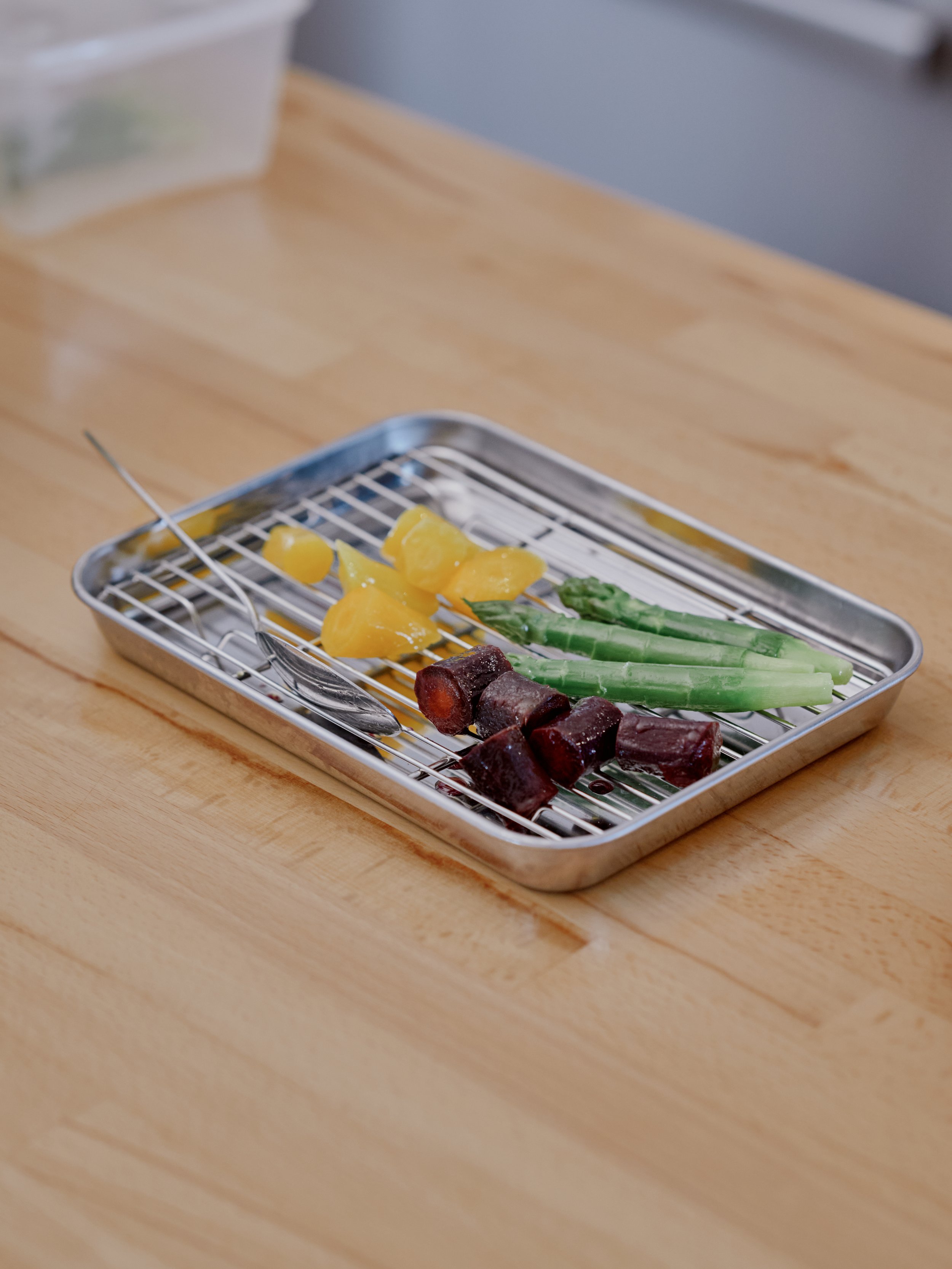 Une plaque en métal avec des morceaux de légumes cuits, including des asperges, des carottes multicolores, sur une surface en bois.
