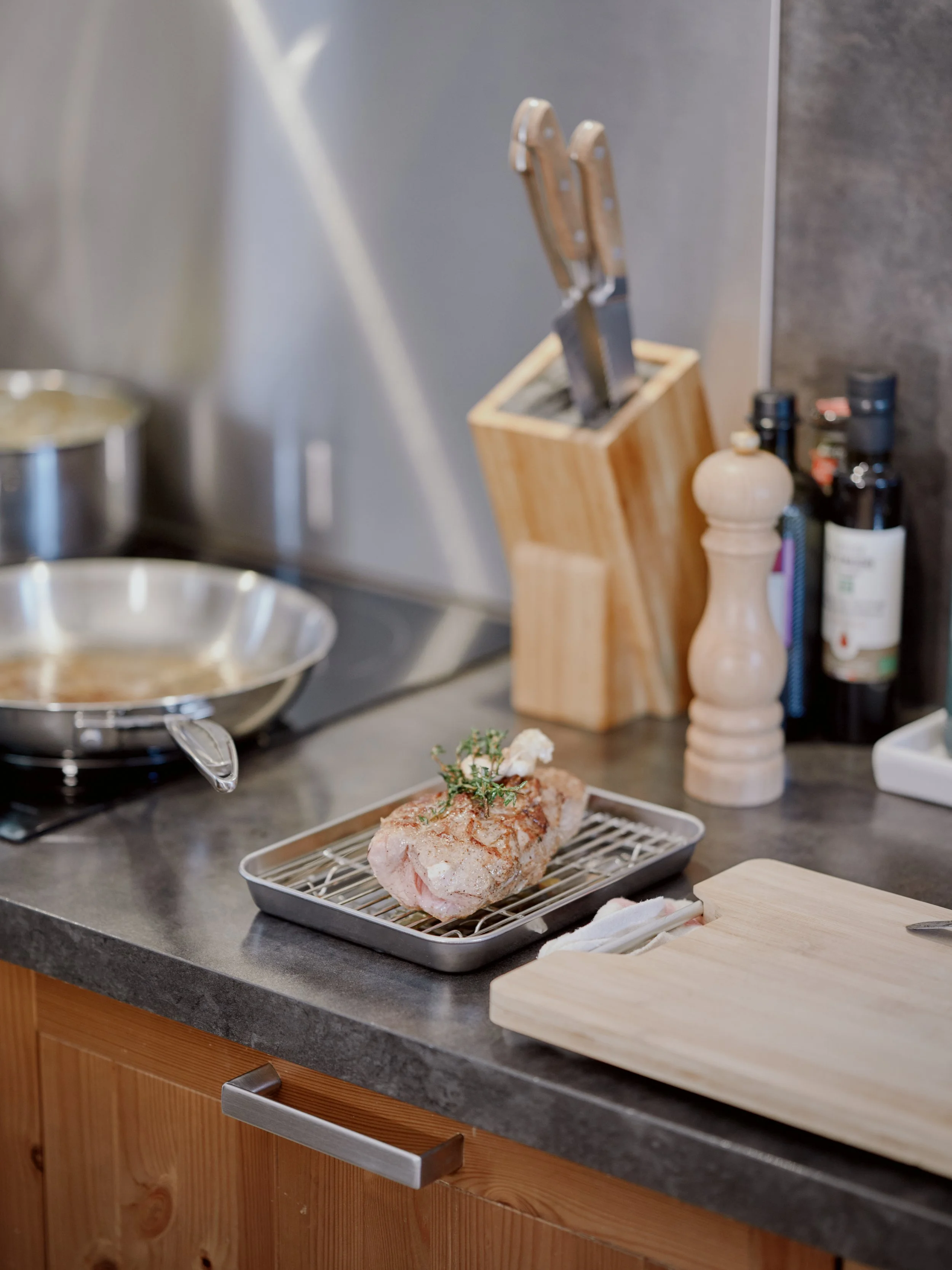 Une pièce de viande poêlée posée sur une grille en métal sur le comptoir de cuisine, entourée d'ustensiles et de condiments.