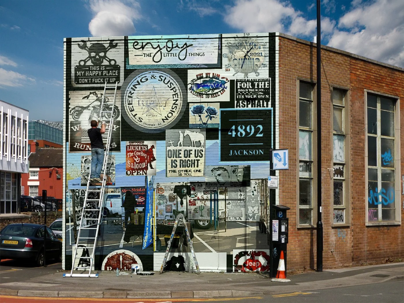 A man is on a ladder adding or adjusting artwork on a mural on a brick building. The mural contains various signs, artwork, and graffiti with messages and images, including a skull and crossbones, a motorcycle, and different words and numbers. The sc