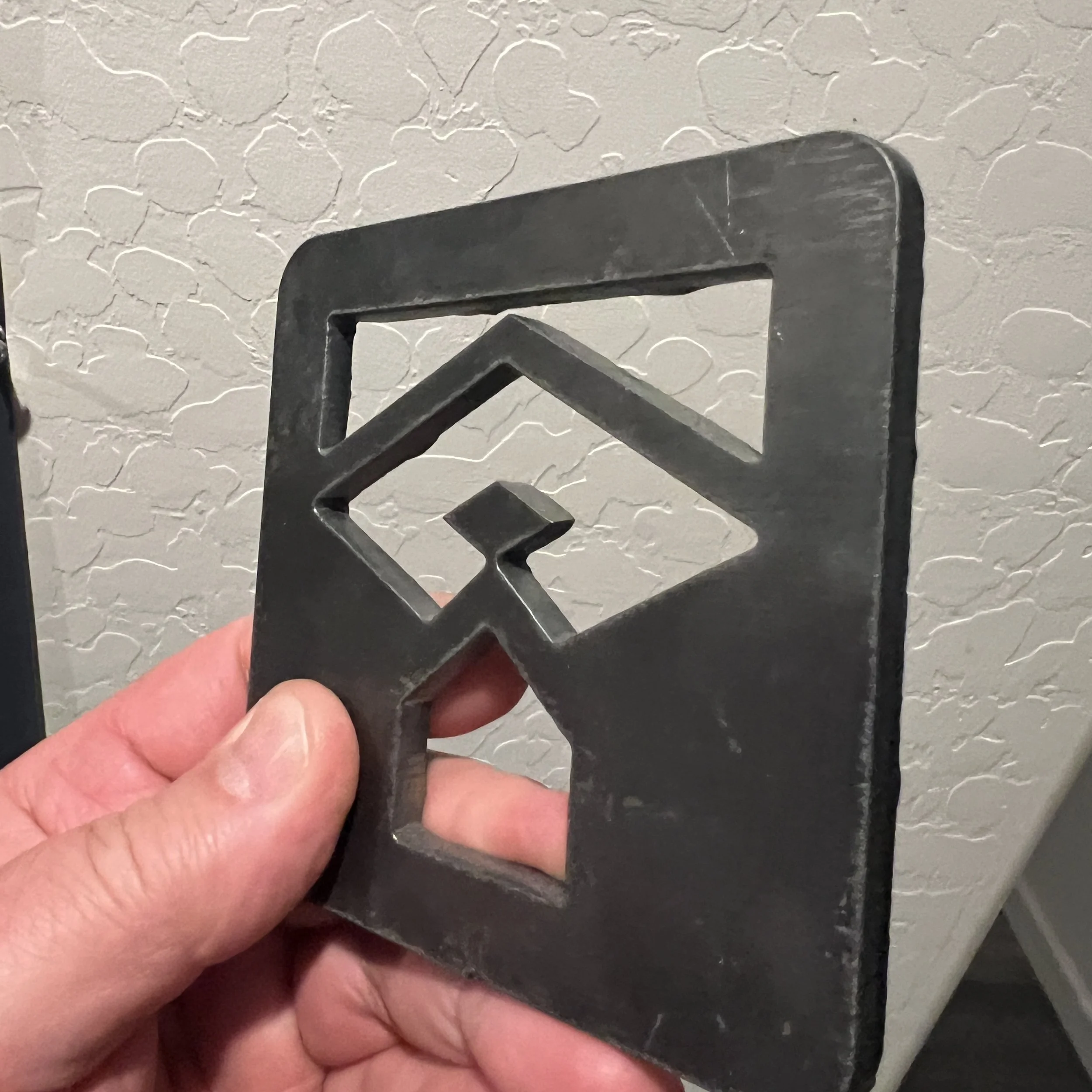 A person's hand holding a small metal square, with a textured wall in the background.
