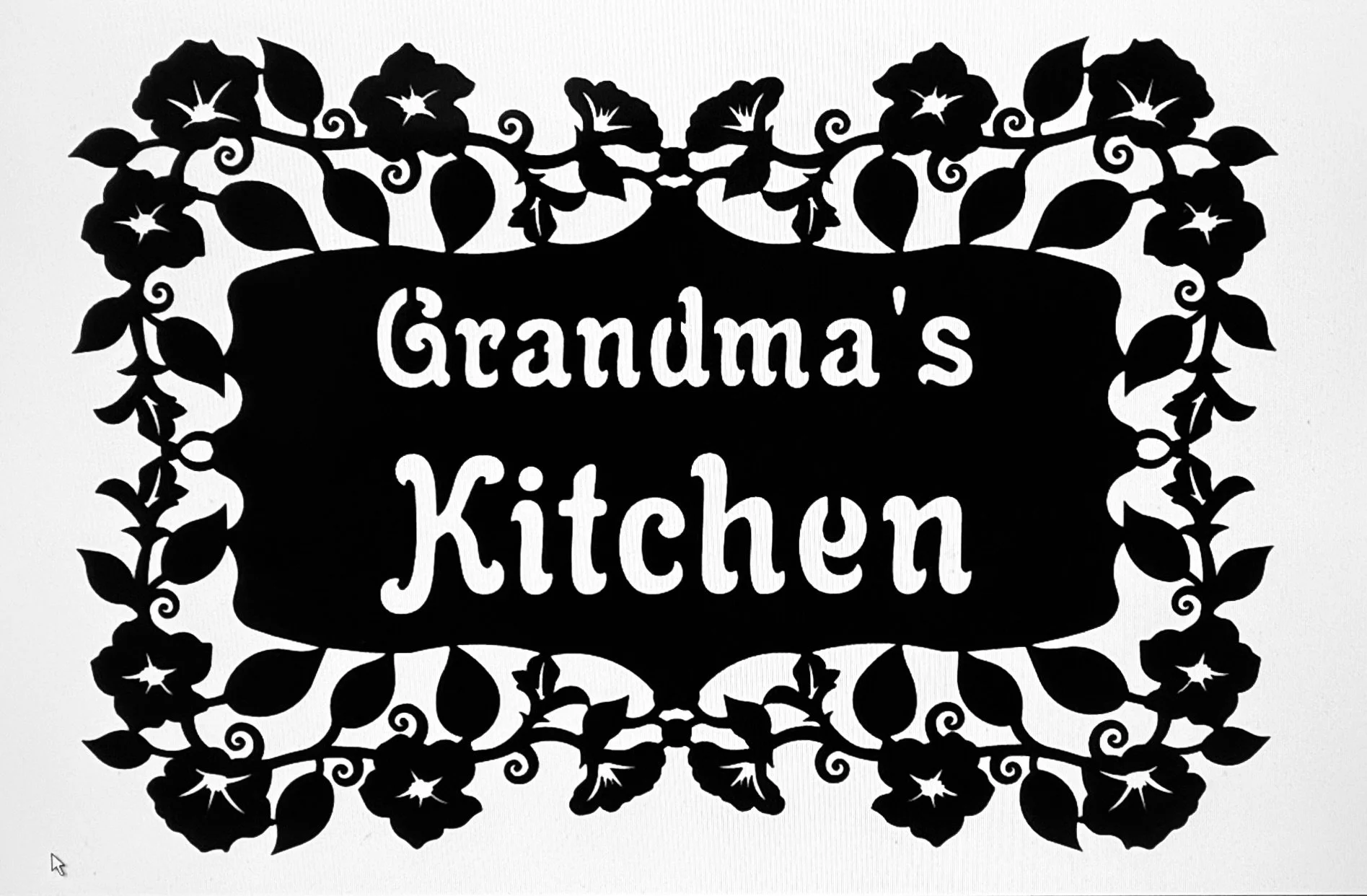 A black and white decorative sign with floral and leaf patterns surrounding the text that reads 'Grandma's Kitchen'.