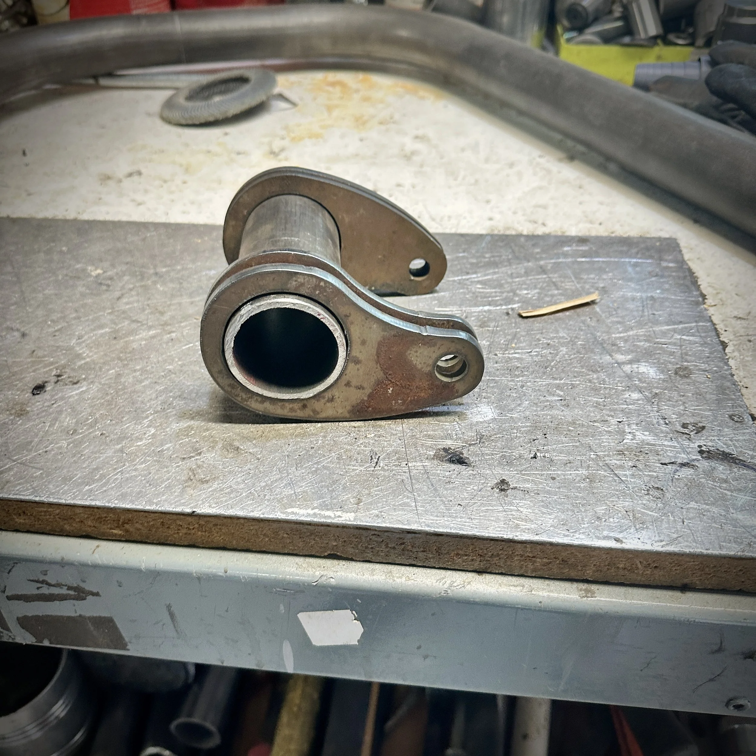 Close-up of a metal component with a cylindrical hollow and a bent arm, situated on a workbench in a workshop.