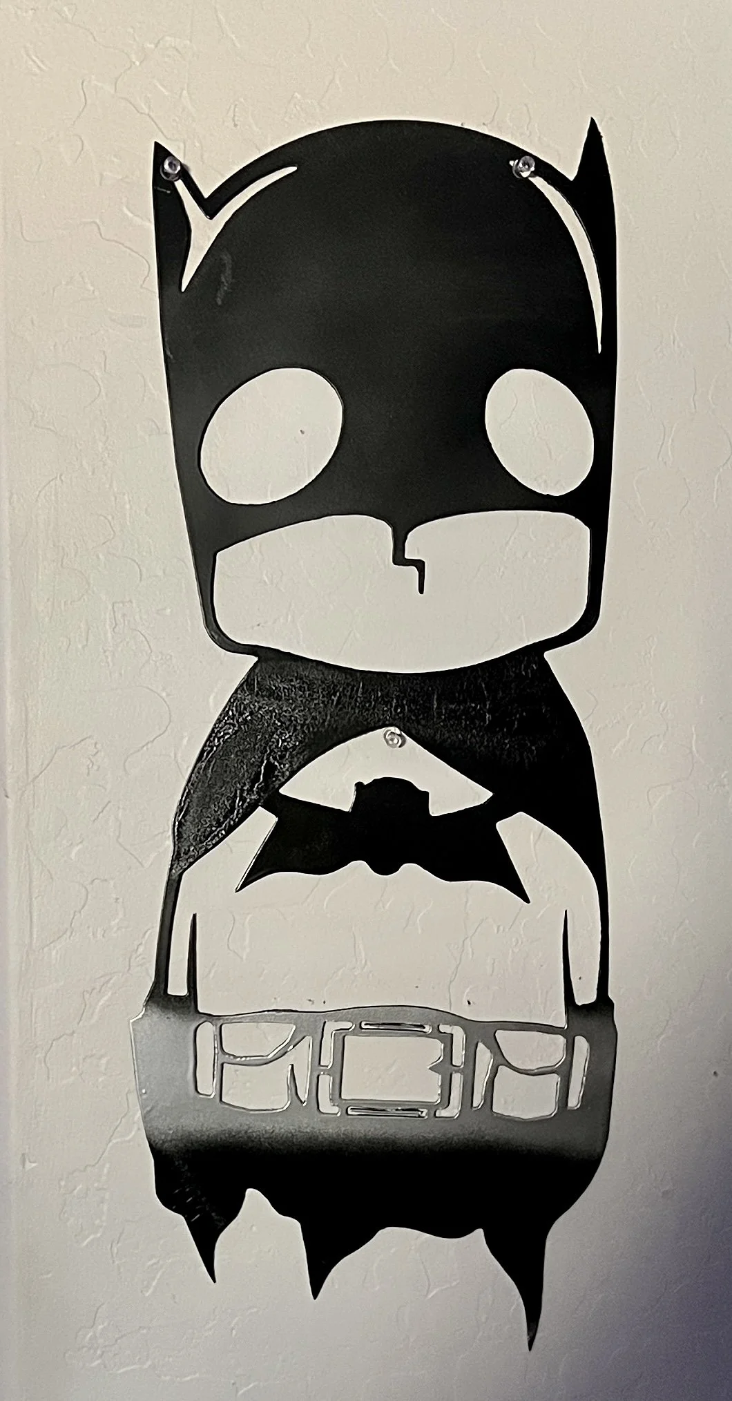 A black and white Halloween decoration of a skull with bat wings, shaped like a spooky cartoon character, hanging on a textured white wall.
