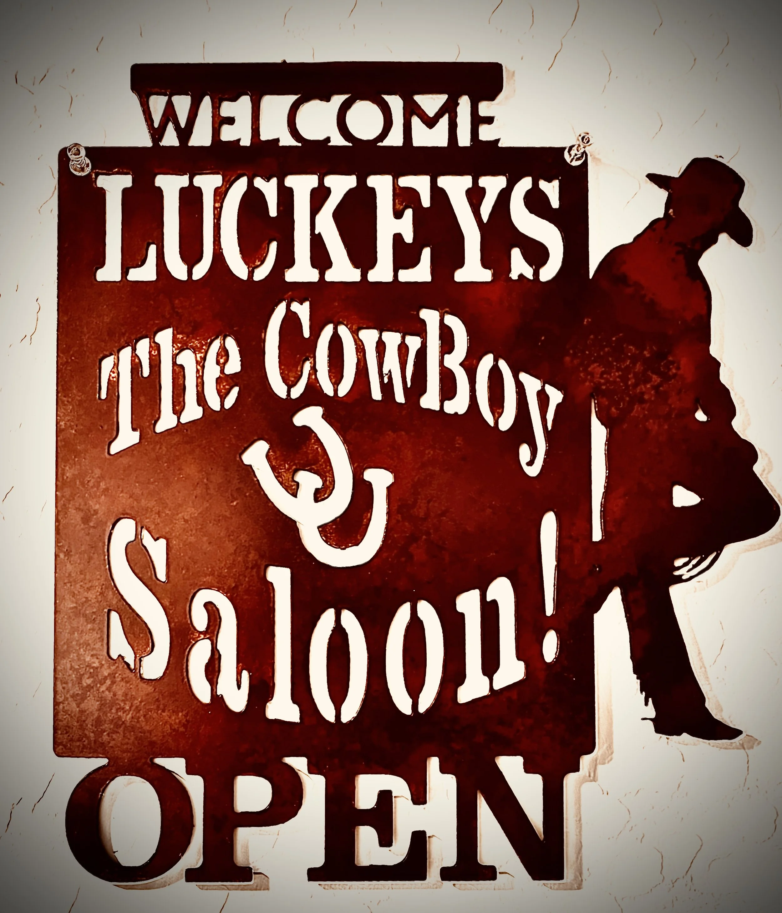 Metal wall decor with the words "Welcome Luckeys the Cow Boy" cut out and a silhouette of a cowboy cowgirl with a hat.