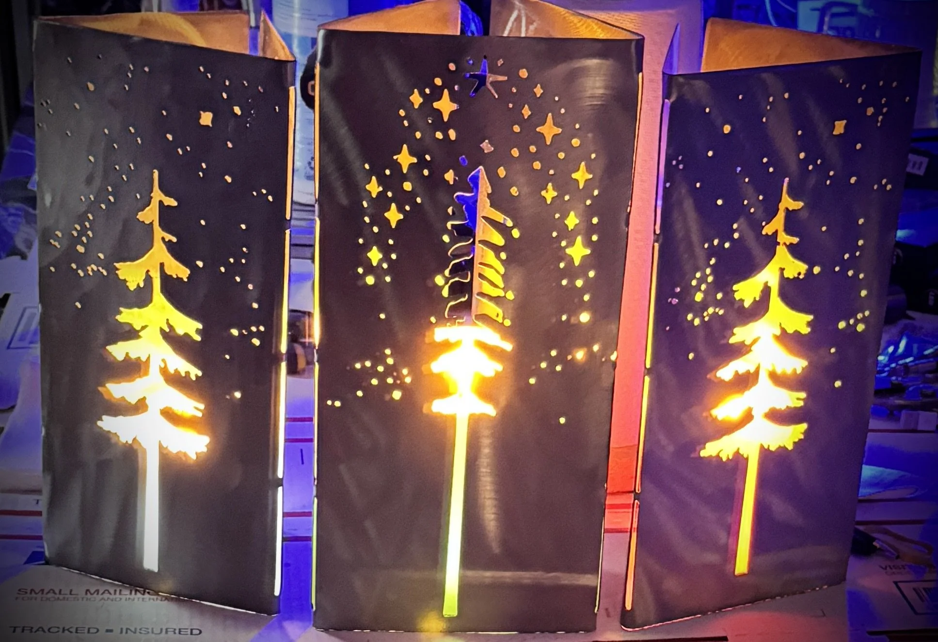 Decorative metal lanterns with Christmas tree cutouts and star patterns, illuminated from within, displayed in a store.