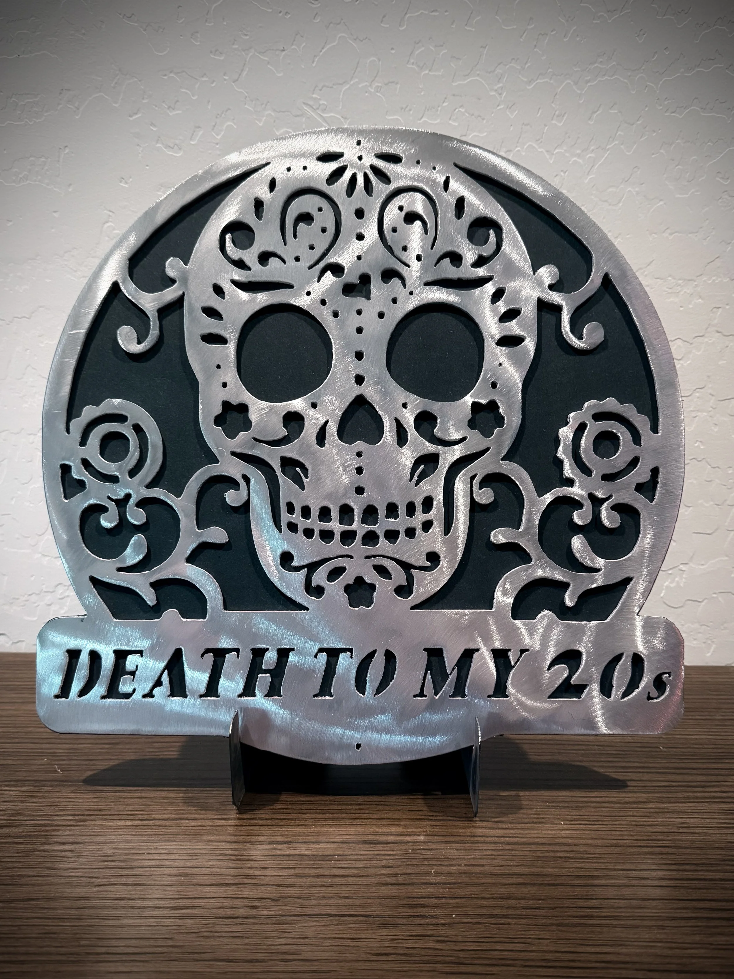 A metallic decorative piece with a skull design and floral patterns. It features the text 'HEALTH TO MY SOULS' at the bottom.