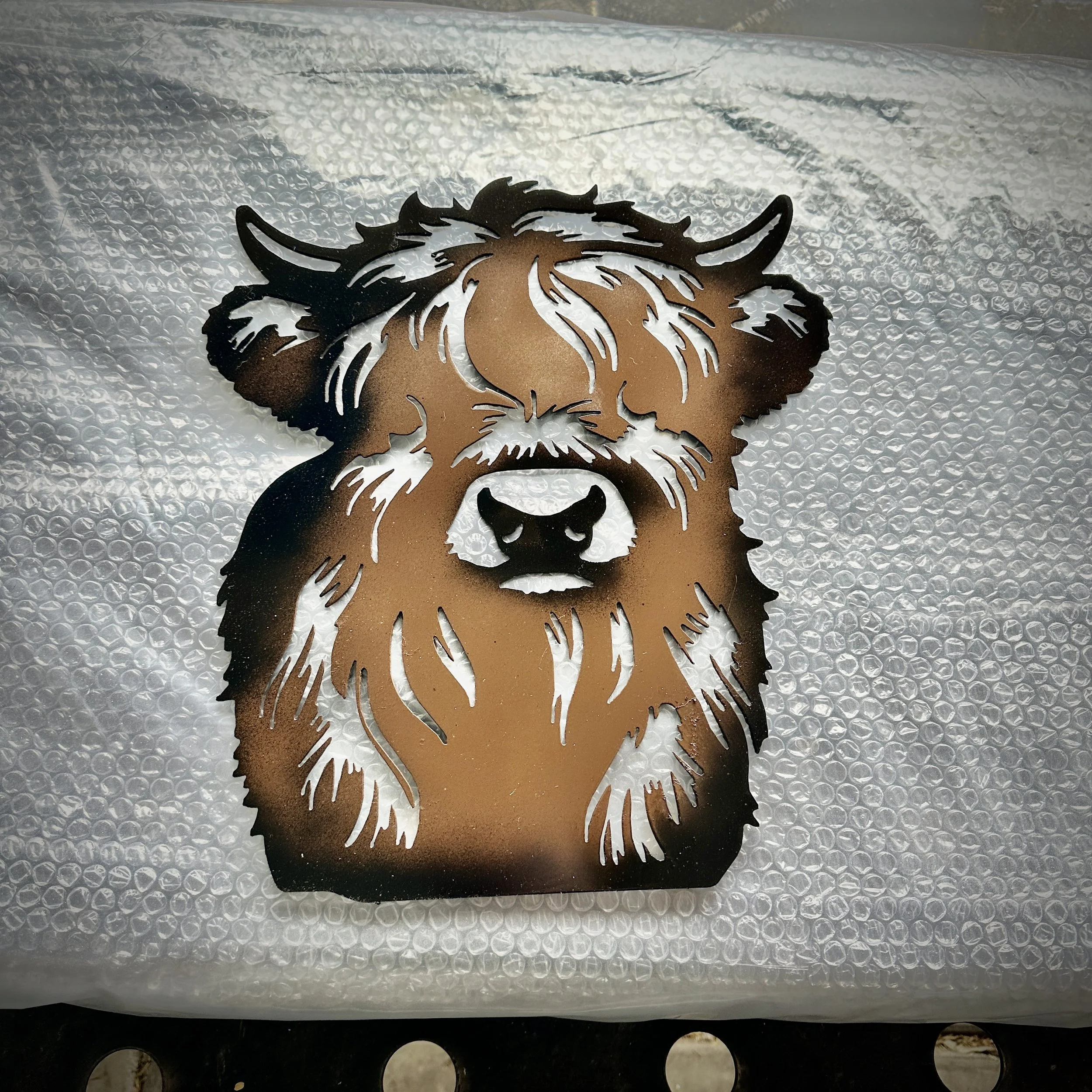 Metal cutout of a bearded man's face with long hair, ears, and a mustache on bubble wrap material.