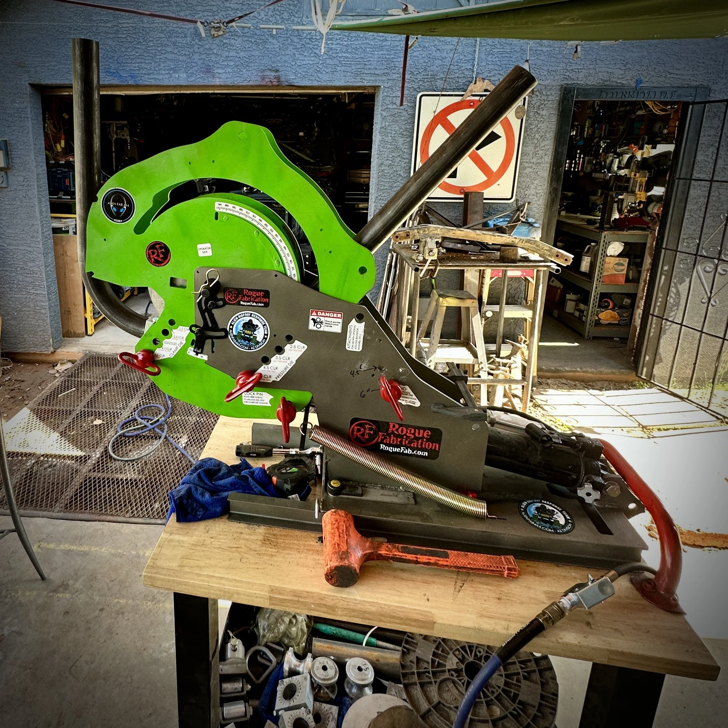 Workshop or garage with various tools, equipment, and storage shelves. Green measuring device or tool prominently displayed in the foreground, with other items including cans, hoses, and workbenches.