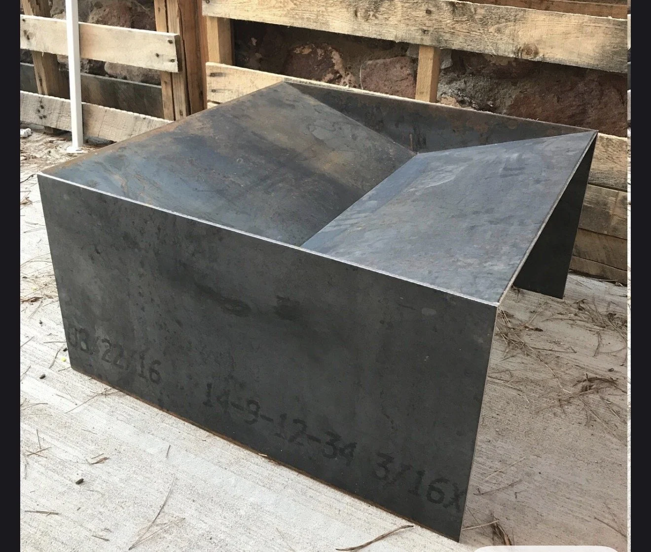 A metal block with engraved numbers and letters resting on a wooden surface at a construction site.
