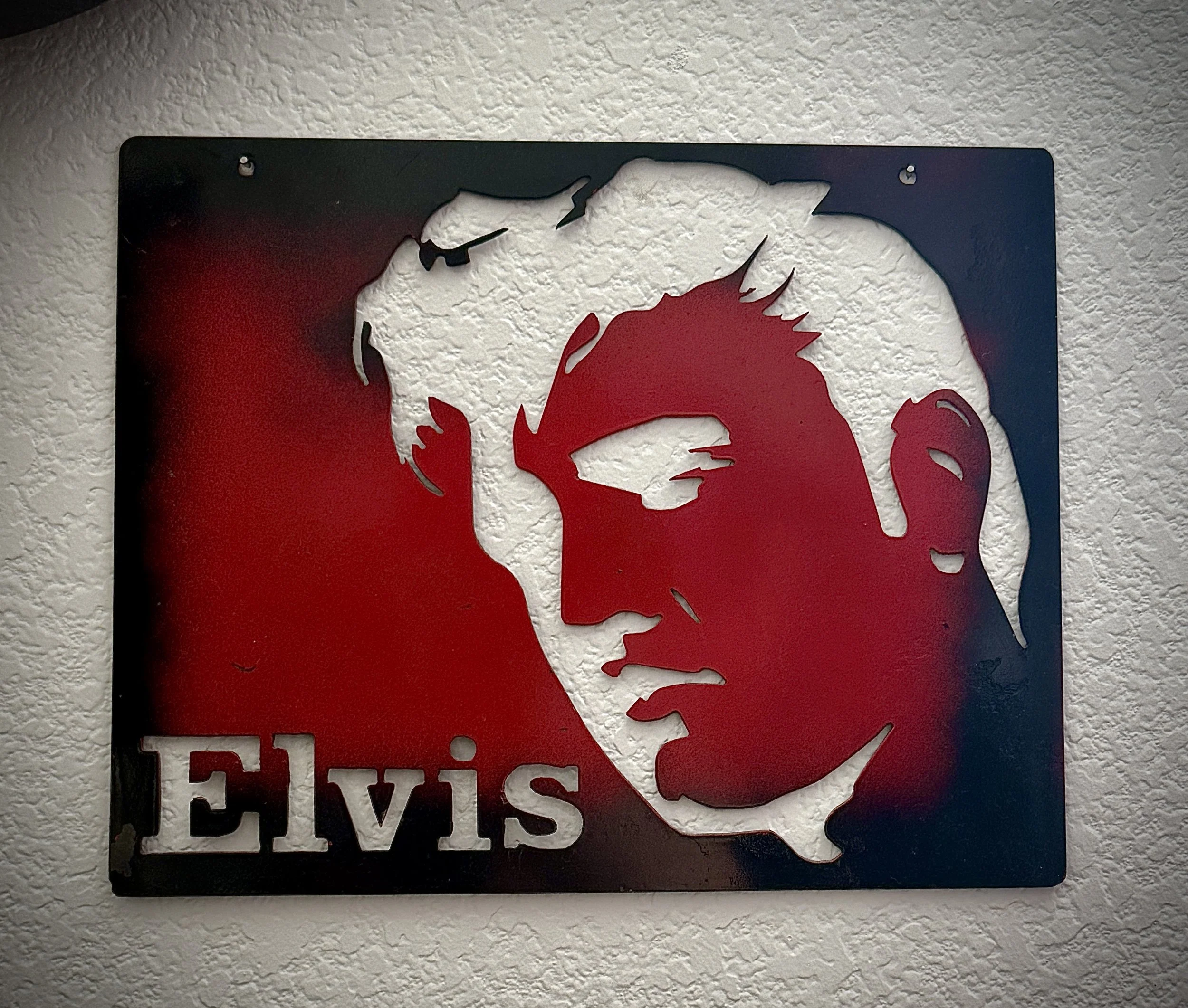 Metal sign with a white lion's face and red mane, with the words 'ELVIS' underneath, mounted on a textured white wall.
