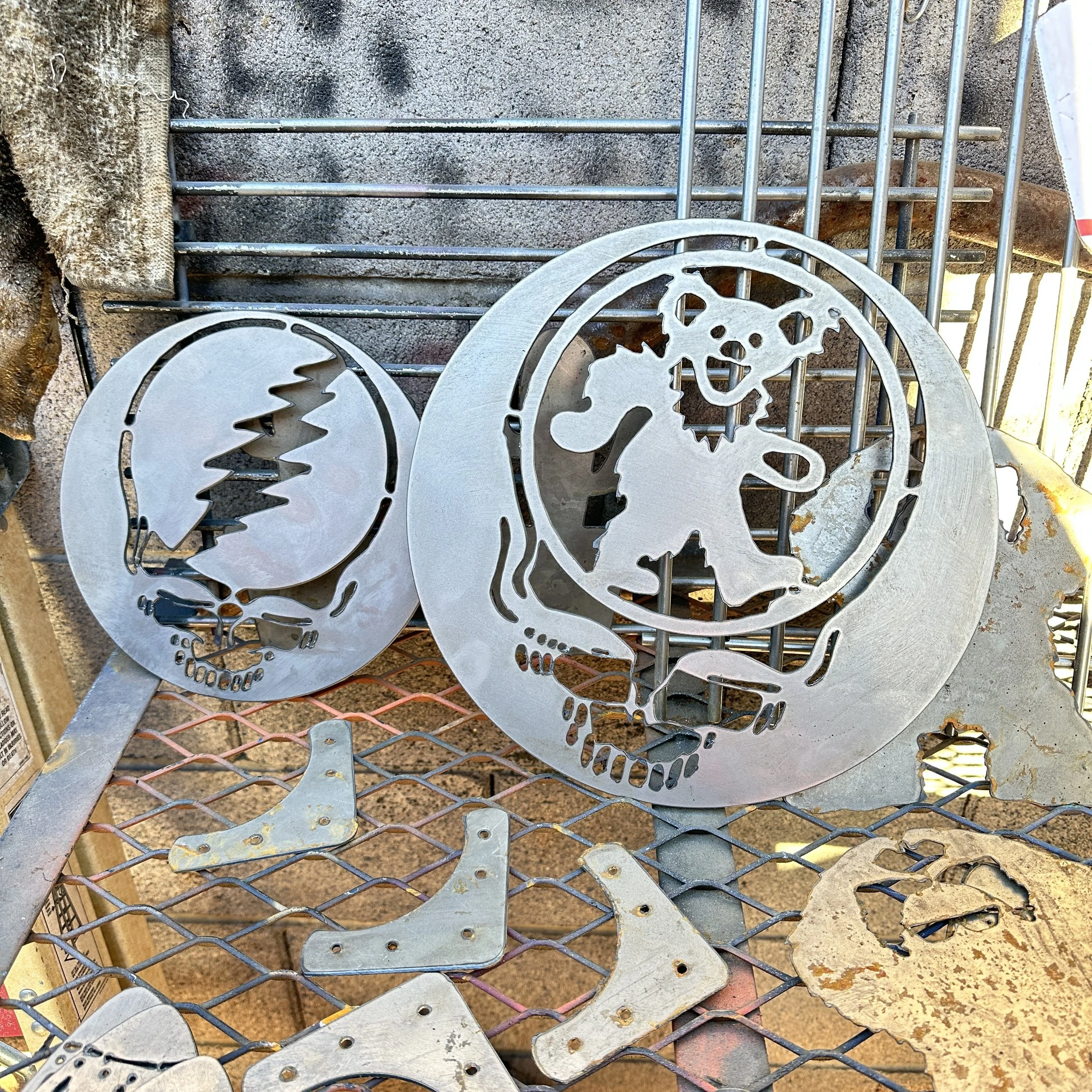 Metal skull silhouette ornaments layered on a wire shelf, with a textured background including a piece of fabric on the left side.