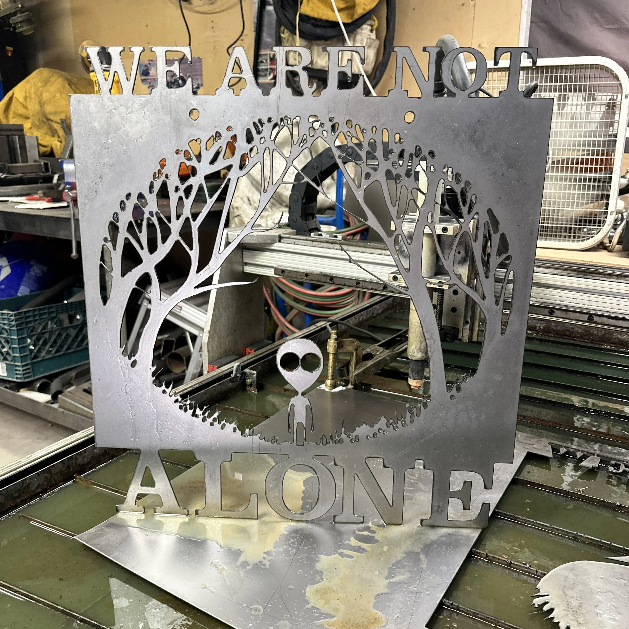 Metal sign with the word "WE ARE NOT" cut out at the top, and a detailed butterfly design at the bottom, on a worktable in a workshop.