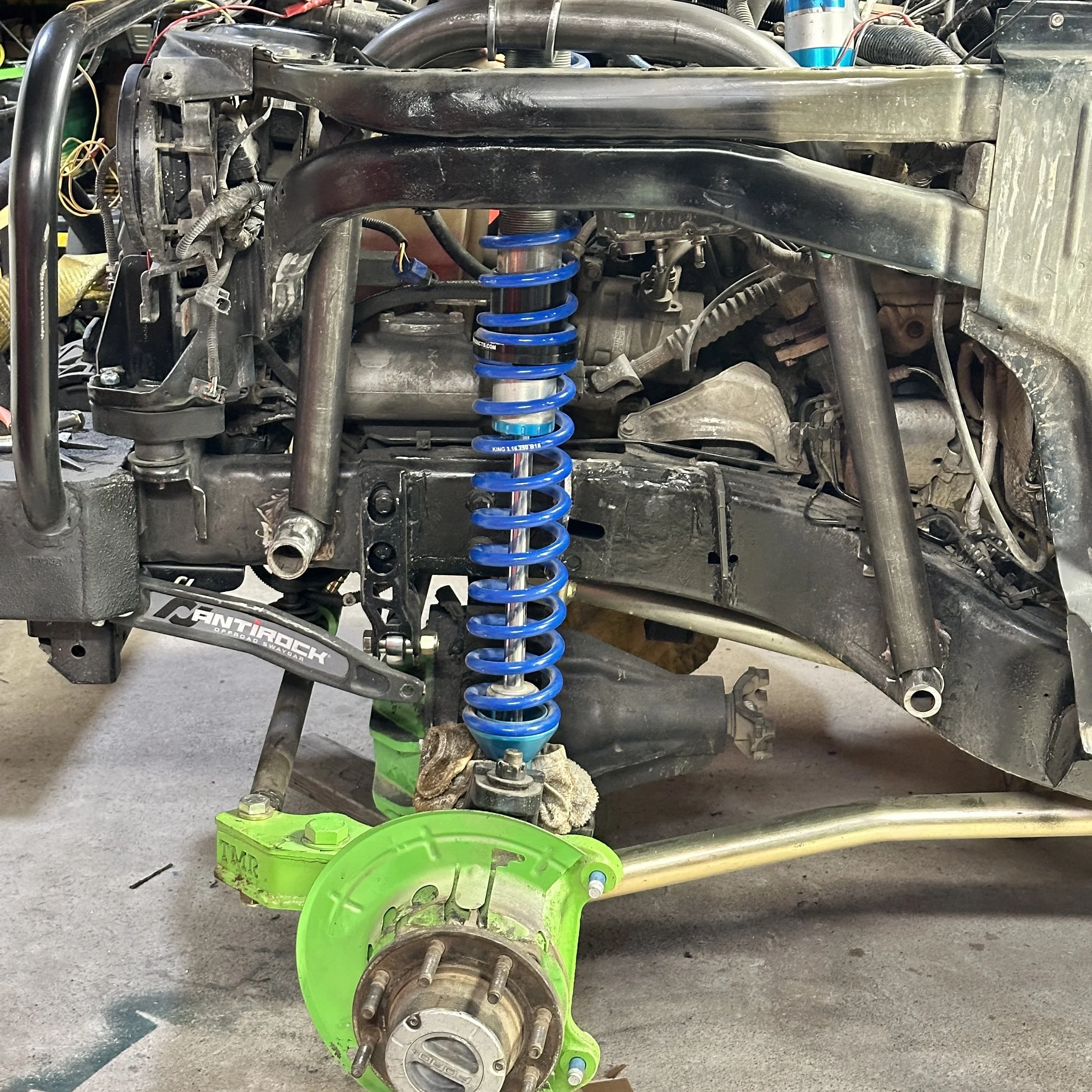 An automobile suspension system with a blue coil shock absorber, removed wheel, and related components, set at a repair shop.