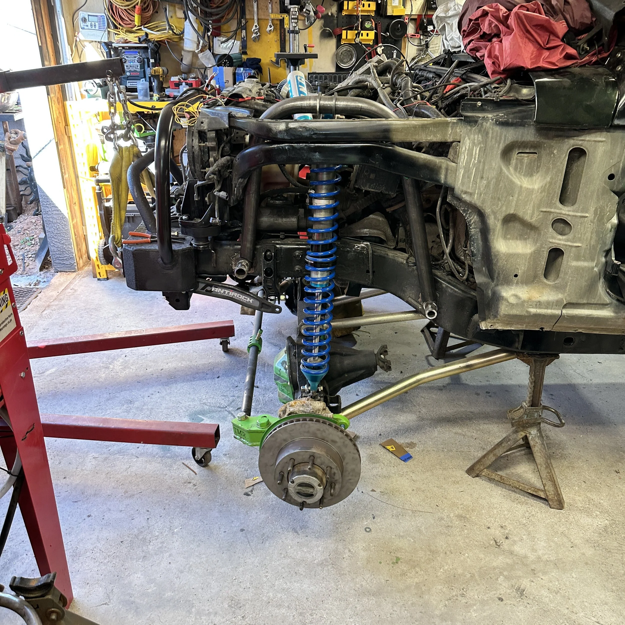 Workshop scene with motorcycle frame and engine parts, tools, and equipment, including a red work light, in the background.